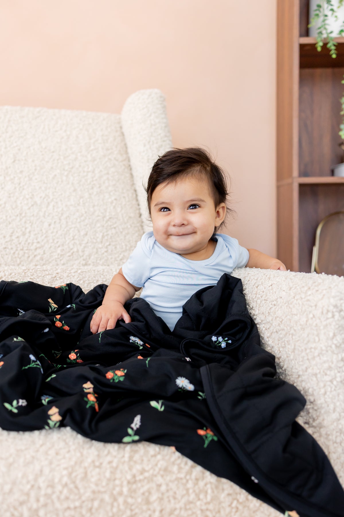 Baby sitting on a white sofa with Baby Blanket in Midnight Wildflower 1.0 print wearing a blue bodysuit