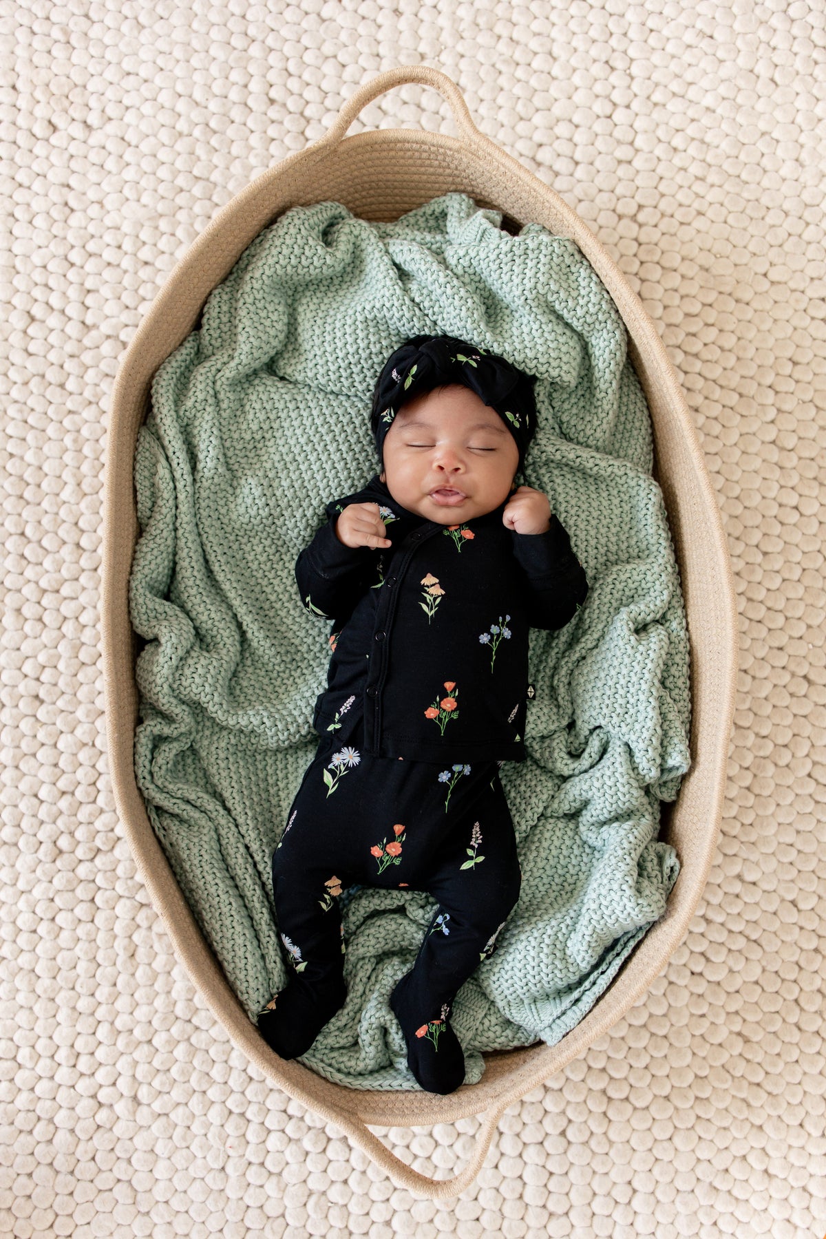 Baby sleeping in a basket wearing Take Me Home Set with Bow in Midnight Wildflower print lying over a green blanket