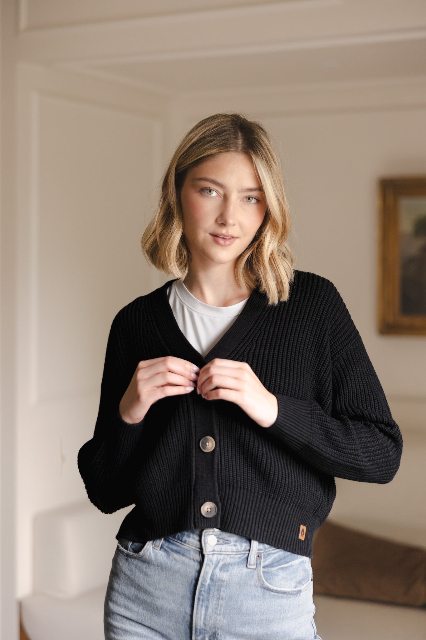 Modal buttoning the Chunky Knit Women's Cropped Cardigan in Midnight over white T-shirt and Blue jeans