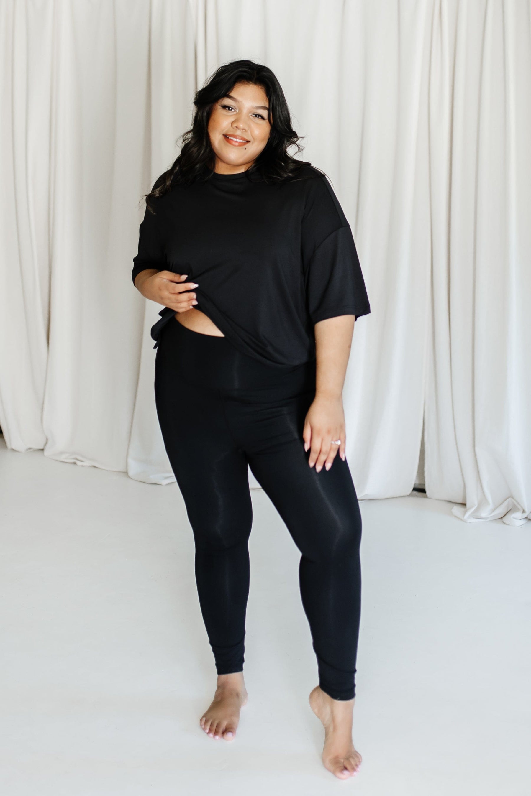 Female model wearing the Bamboo Flex Women’s Leggings in Midnight and the short sleeve tee standing in front of a cream backdrop