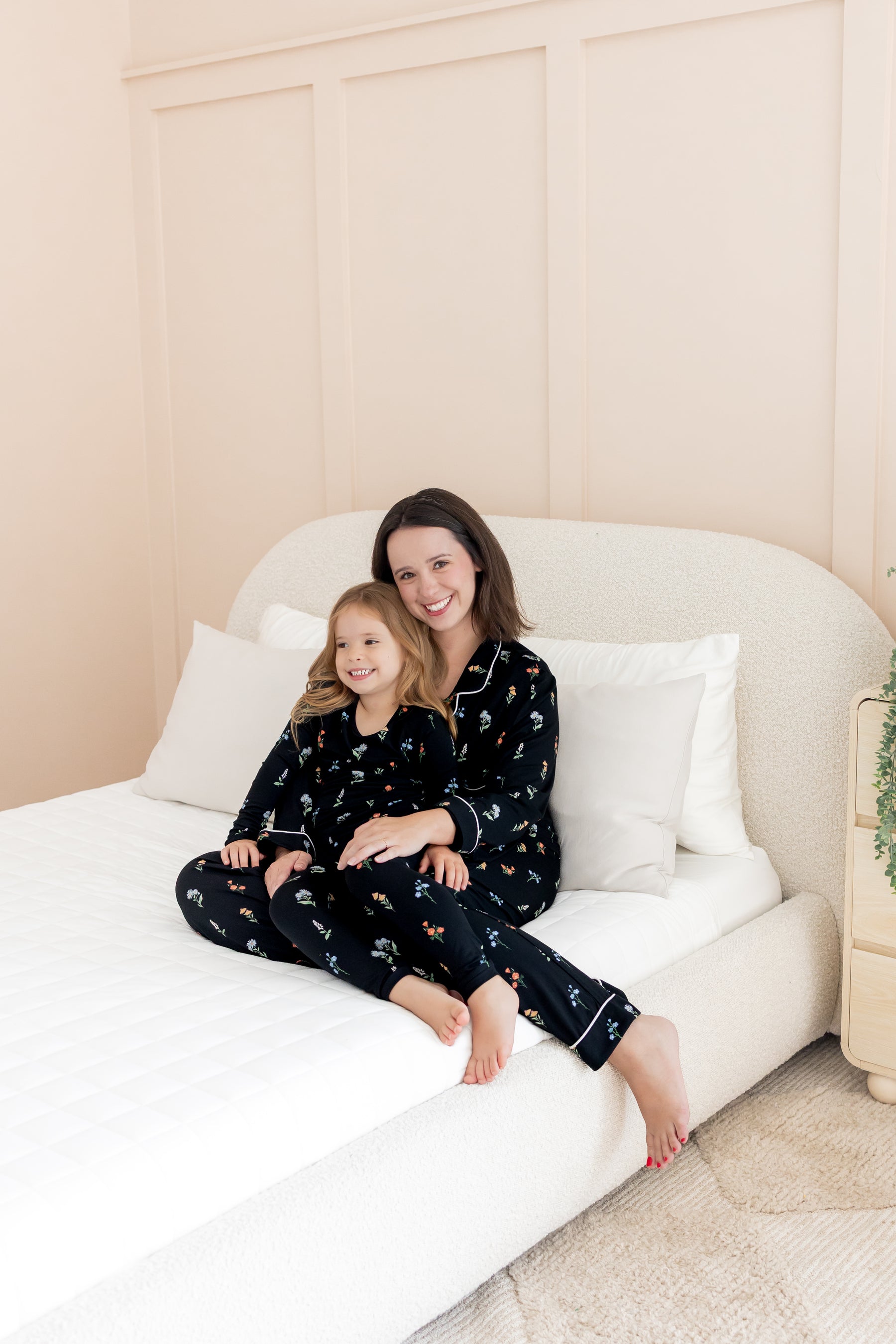 Model and girl wearing matching long sleeve pajama sets in midnight wildflower print cuddling on white bed