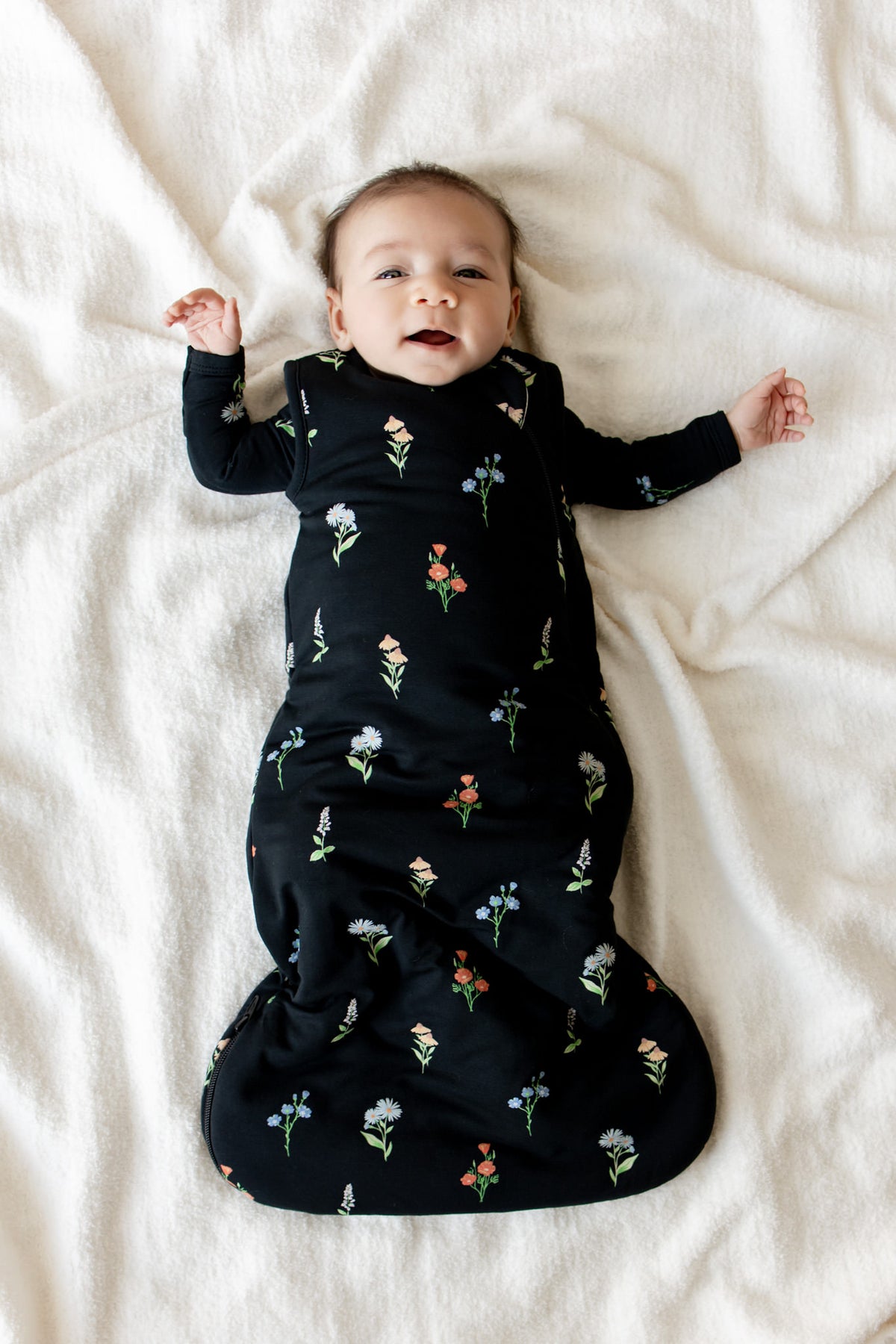 Baby lying on a white sheet wearing Sleep Bag in Midnight Wildflower 1.0 print