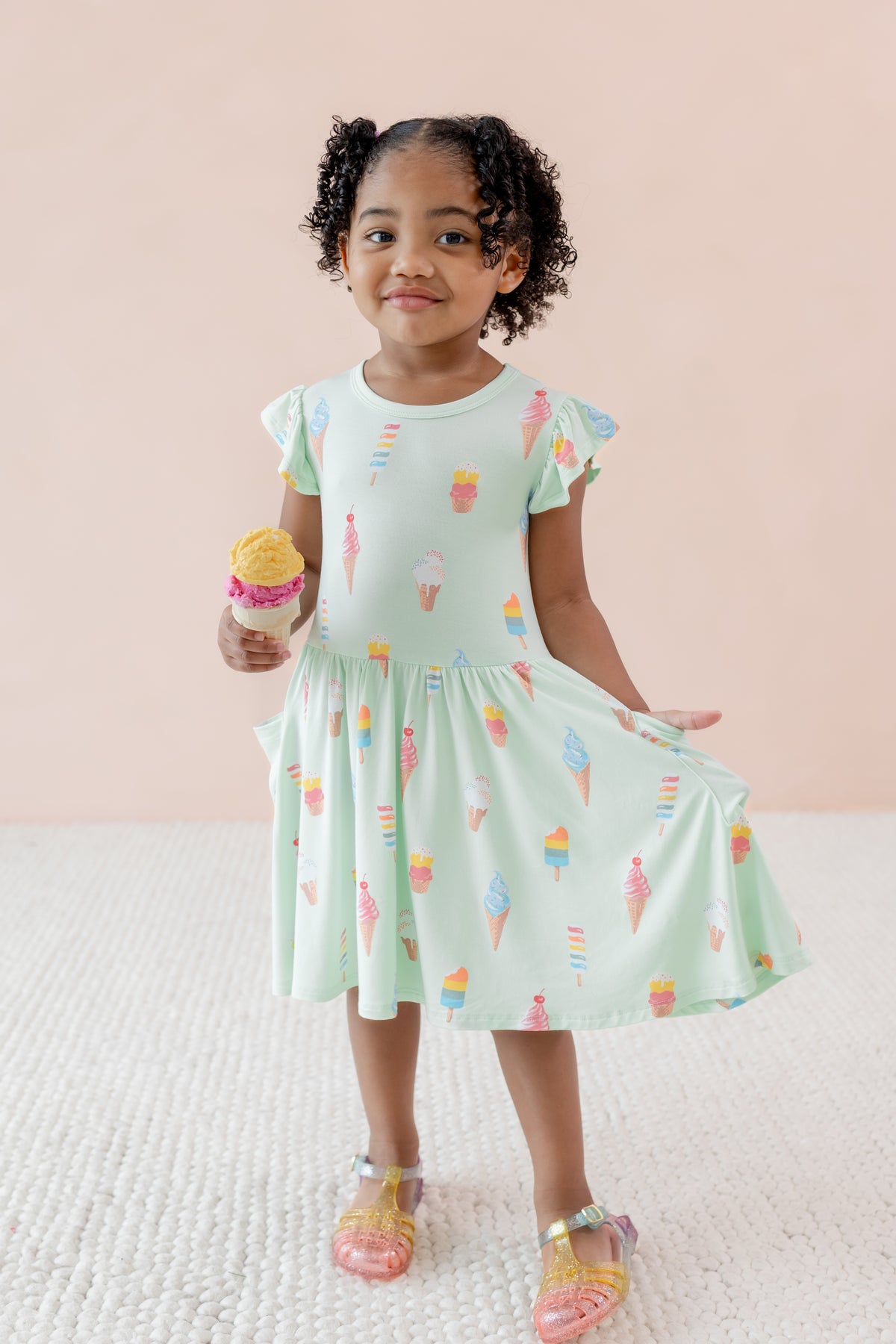Child wearing Mint Ice Cream print  Pocket Dress with sandles on a beige background holding an ice cream