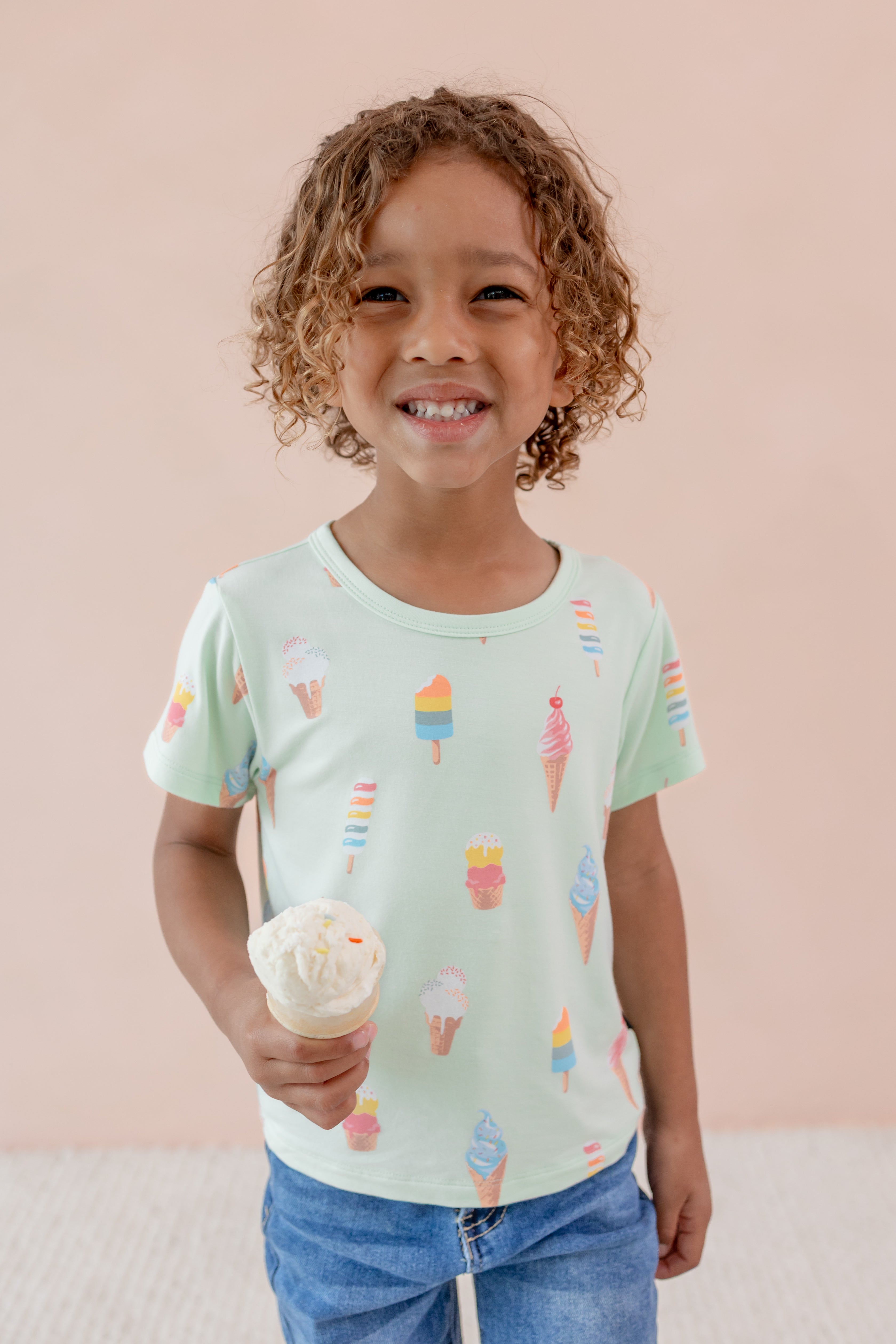 Child smiling holding an ice cream cone wearing Toddler Basic Tee in Mint Ice Cream over Denim pants print on a beige background