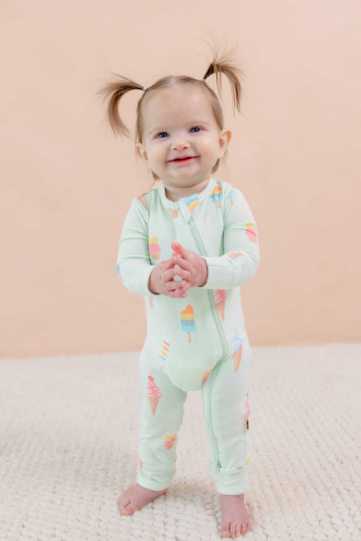 Child wearing a light green zippered onesie with colorful ice cream patterns on a beige background