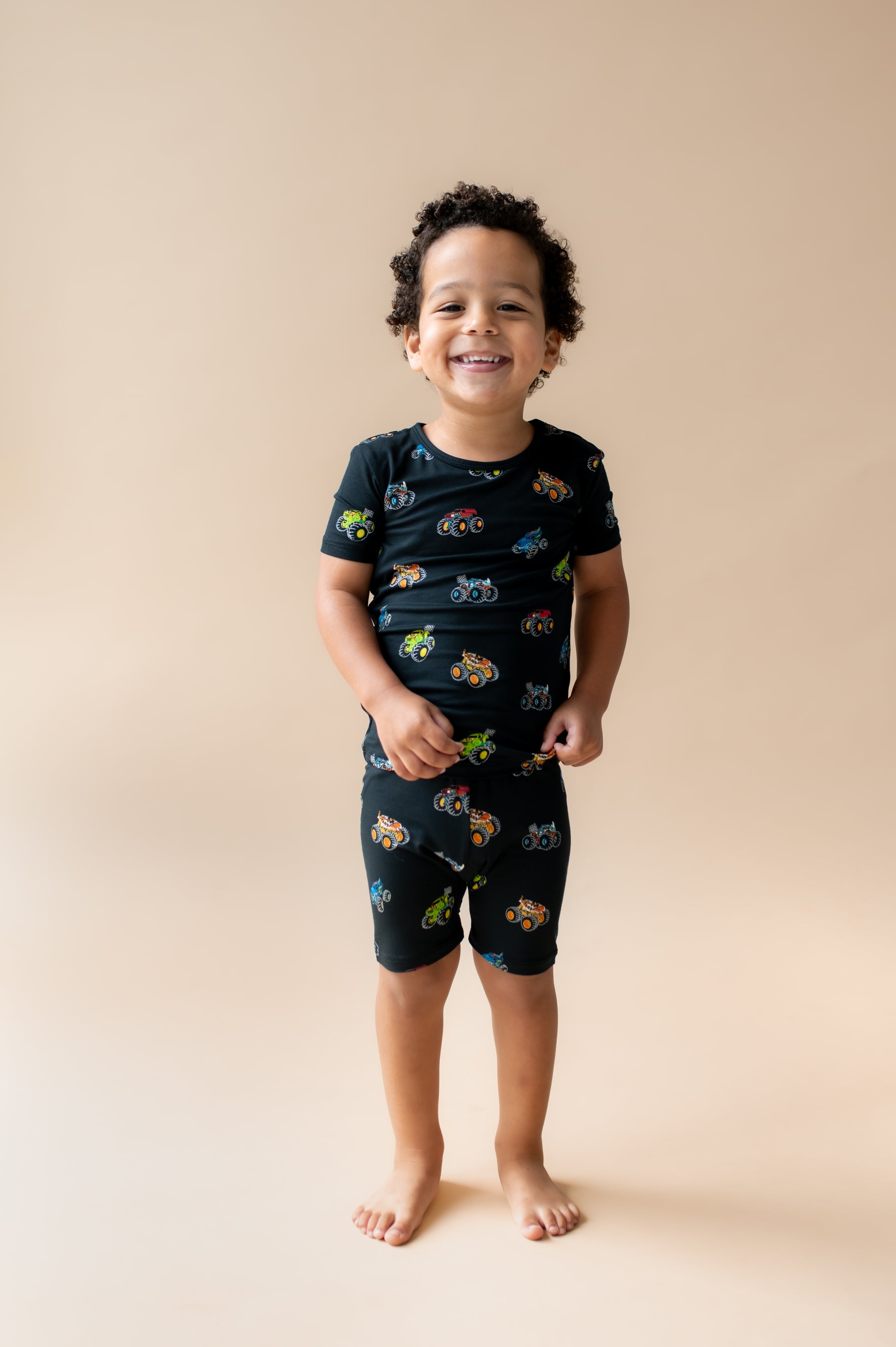 Boy wearing Black Short Sleeve Pajamas in Monster Truck print on beige background