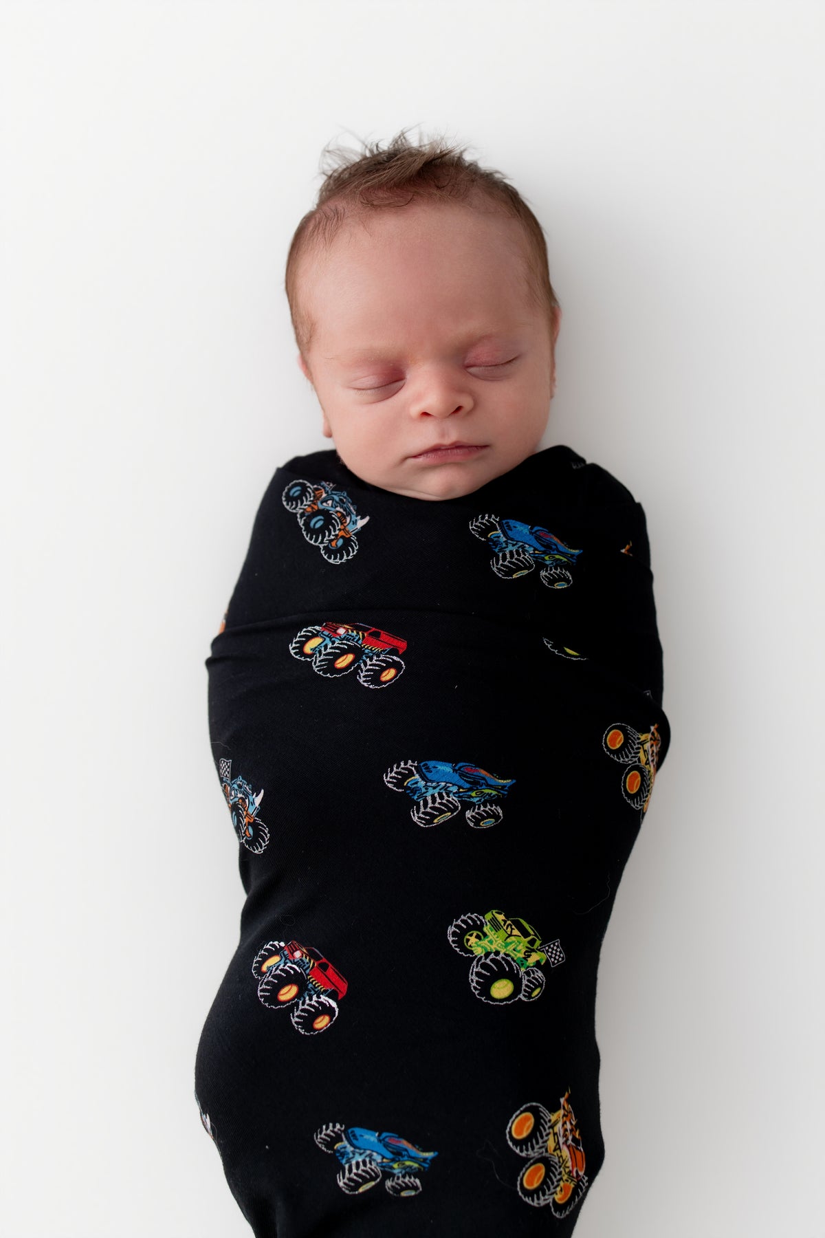 Baby sleeping in Black Swaddle Blanket in Monster Truck print on white background