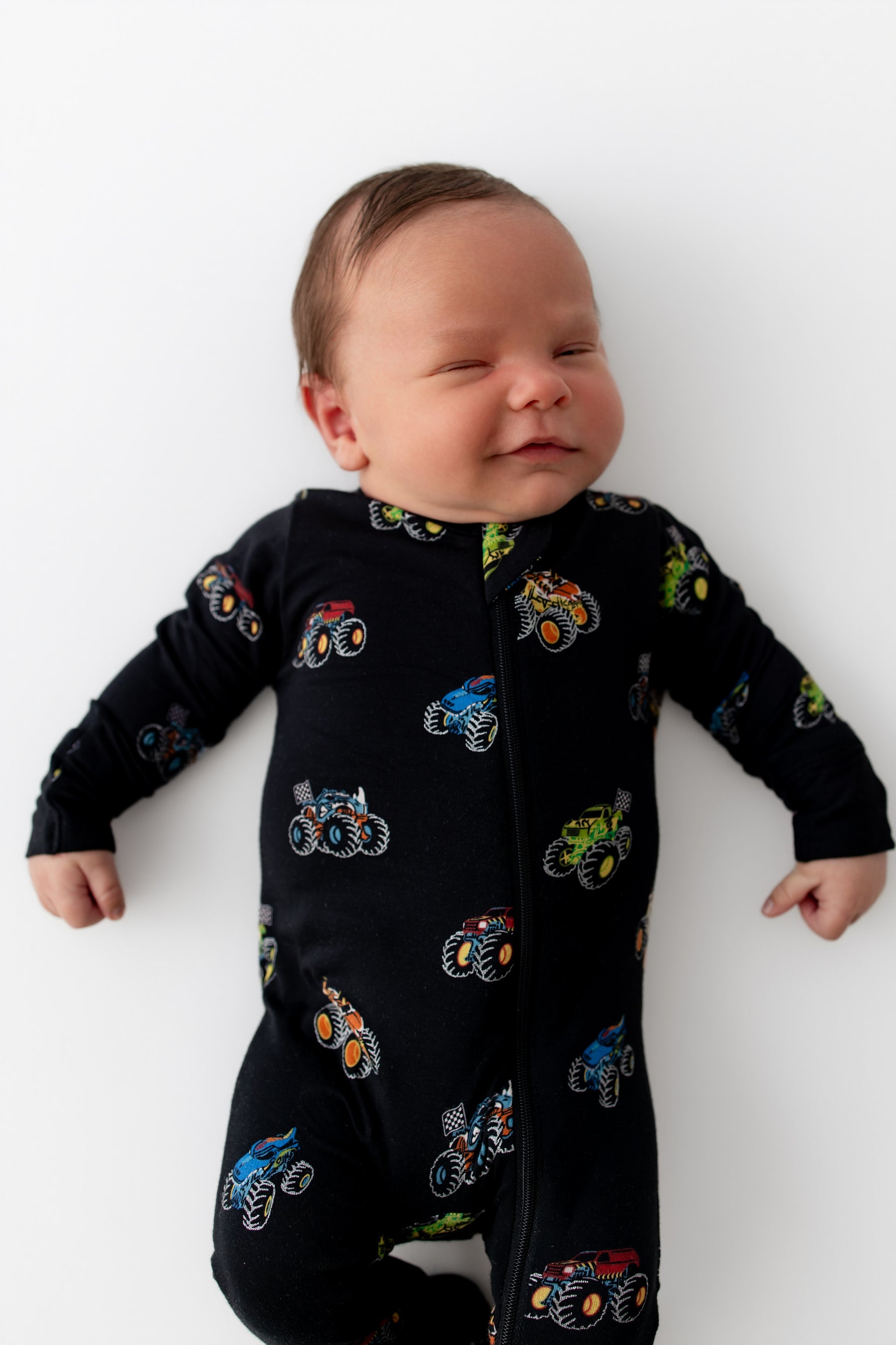 Baby wearing Black Zippered Footie in Monster Truck print on white background