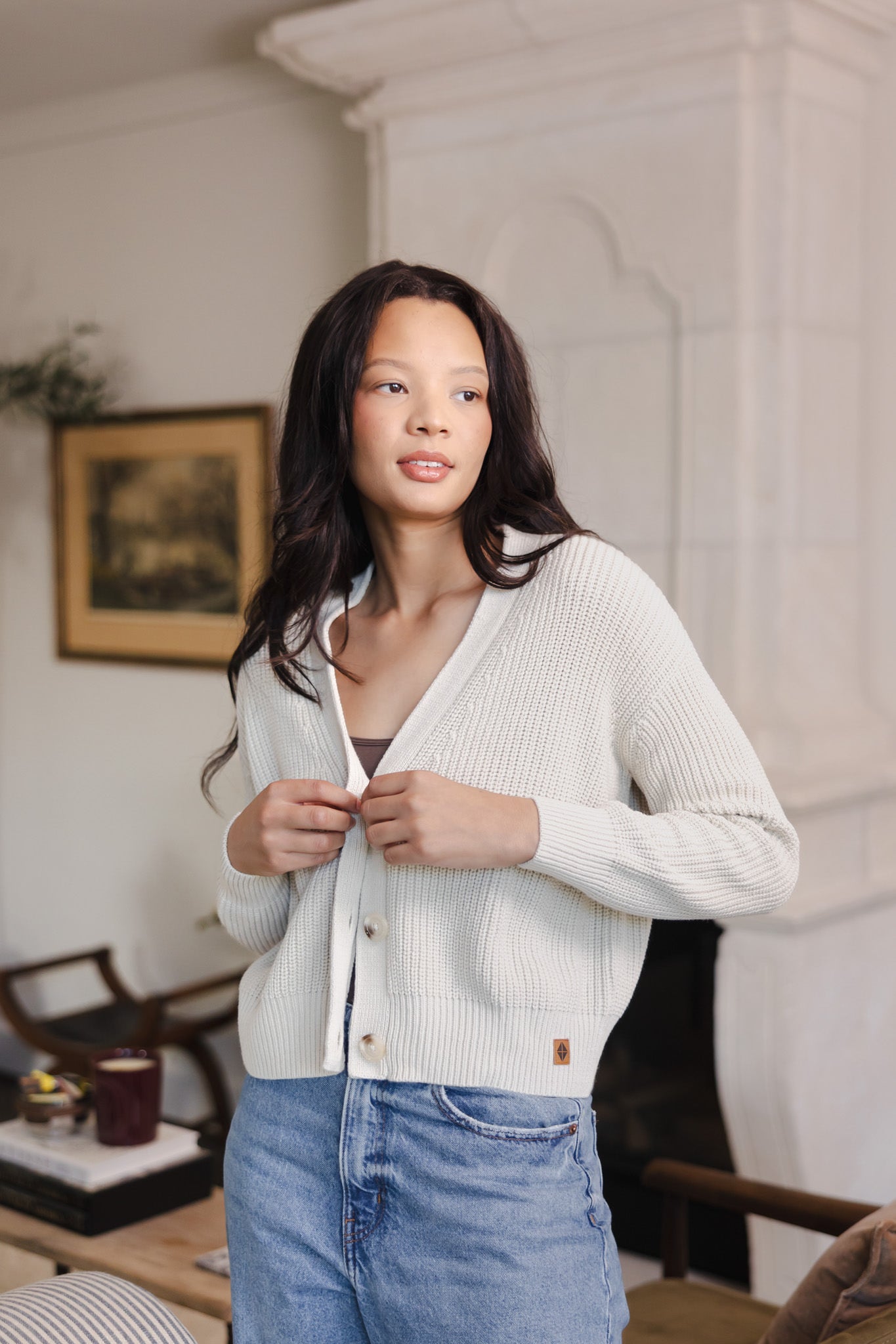 Modal buttoning the Chunky Knit Women's Cropped Cardigan in Oat over blue jeans