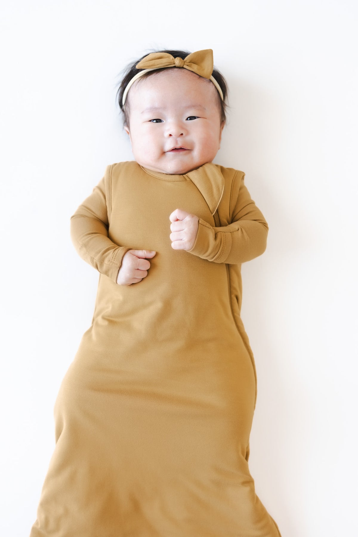 A baby wearing a mustard yellow wearable blanket and bow