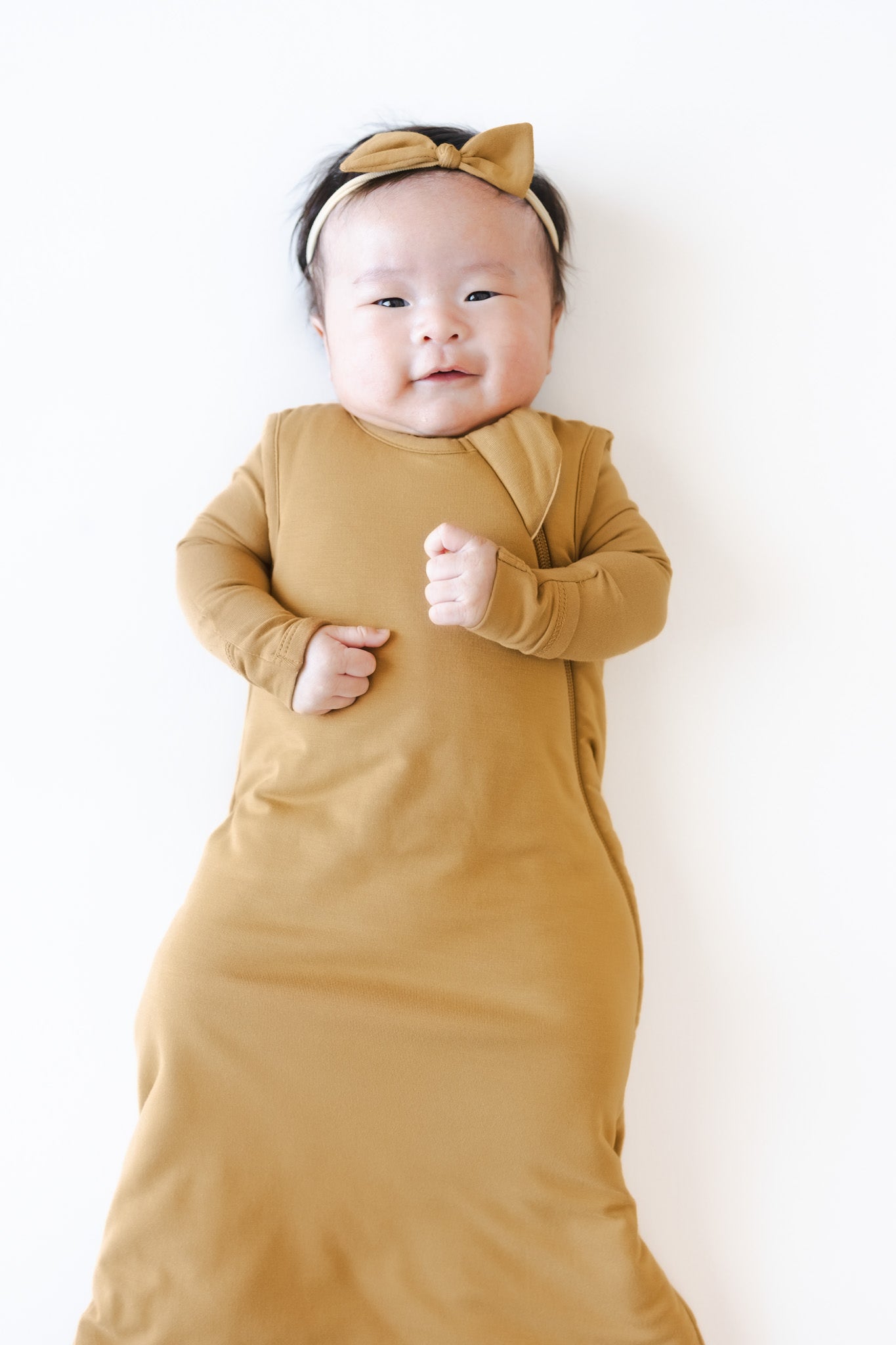 A baby wearing a mustard yellow wearable blanket and bow