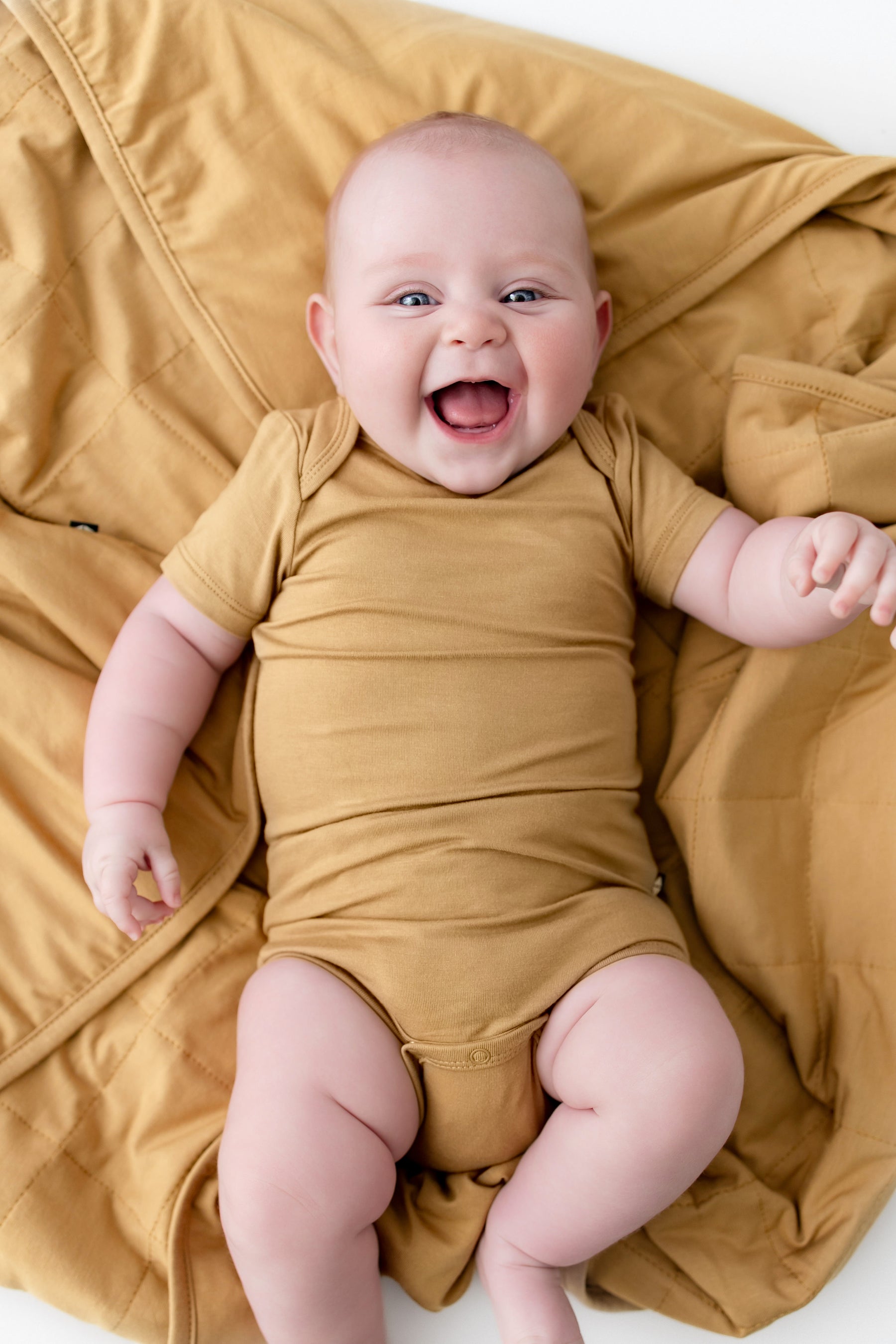 Close up of Baby lying over Baby Blanket in Ochre wearing a similar color bodysuit on a white background