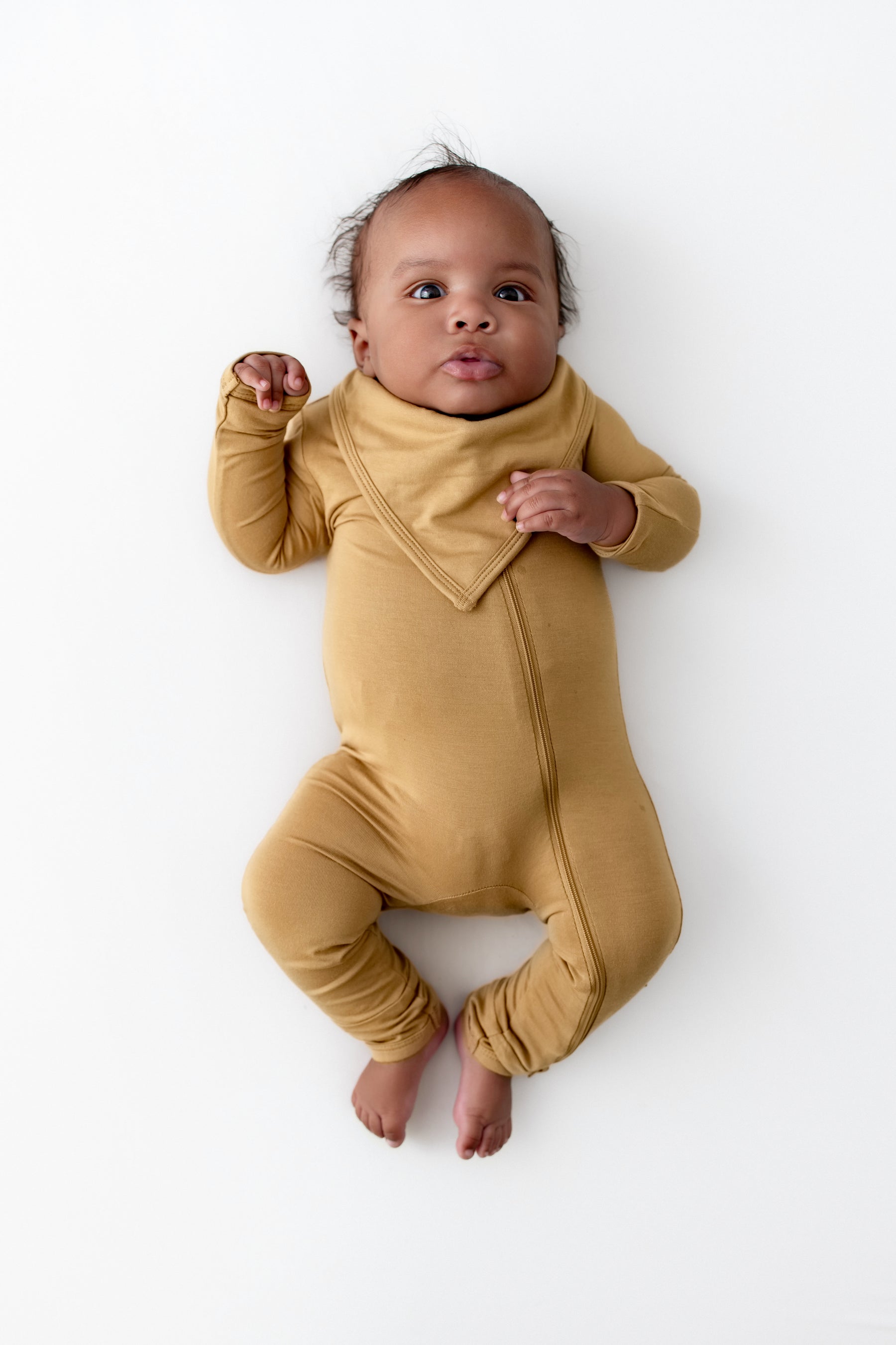Baby wearing Bib in Ochre over zippered romper in Ochre on a white background