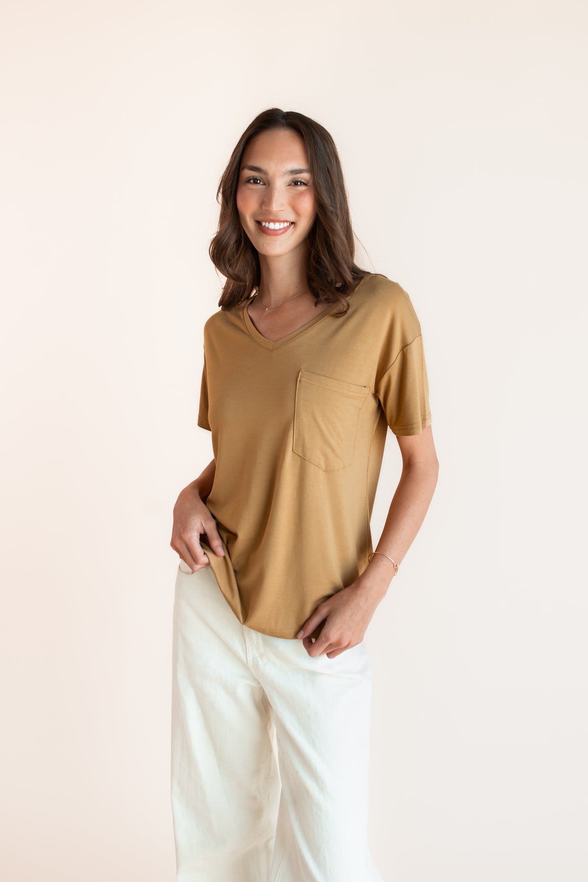 Model wearing Women's Oversized V-Neck Tee in Ochre over white pants on a beige background