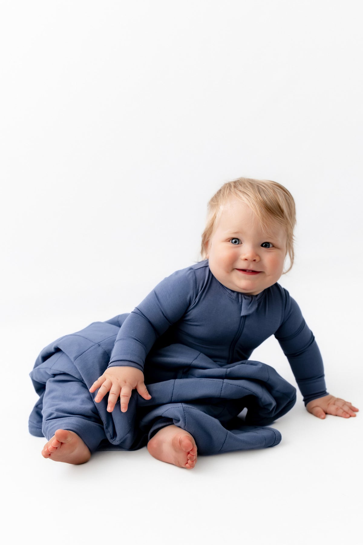 Baby sitting with Baby Blanket in Oxford wearing a similar color zippered romper on a white background