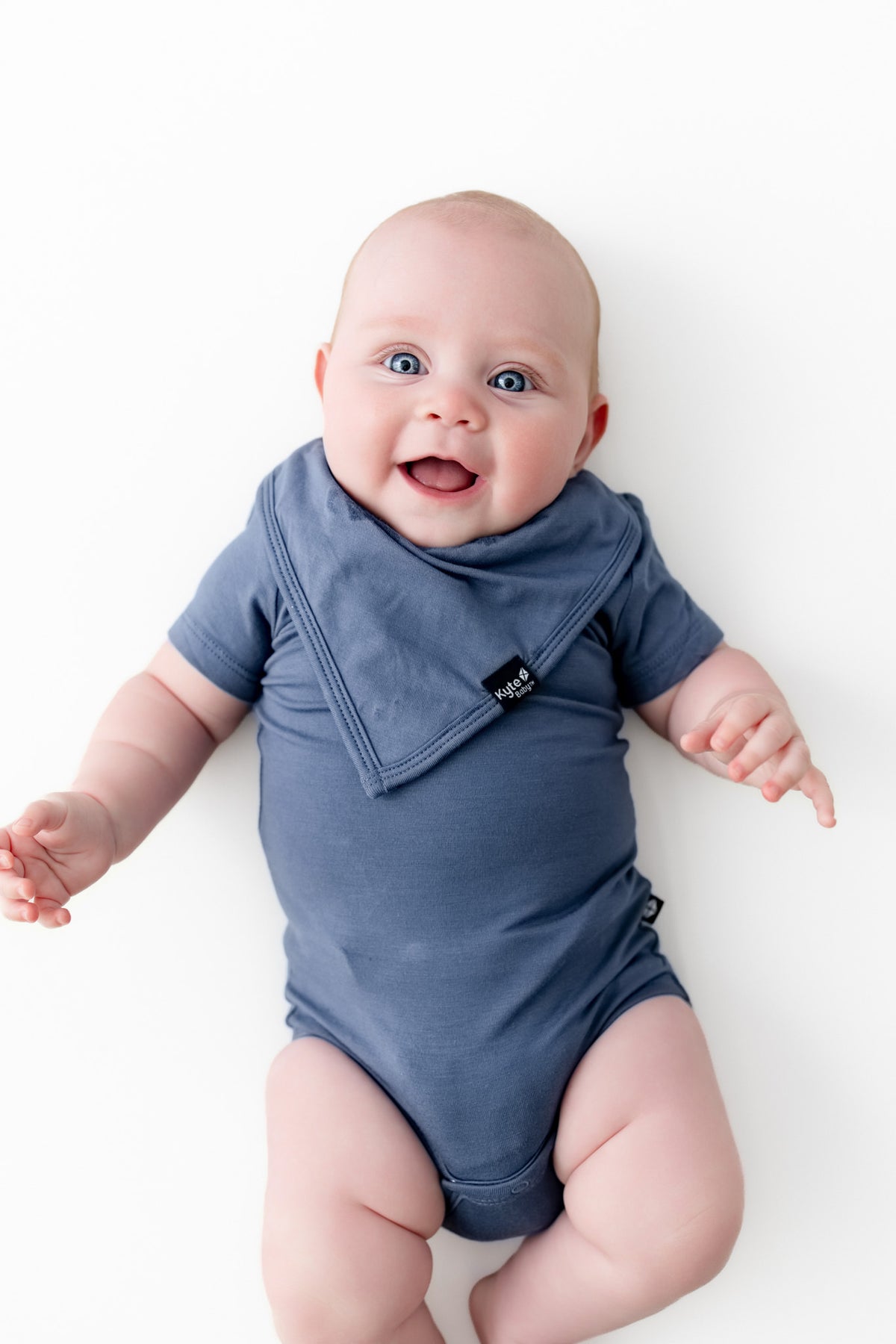 Baby wearing Bib in Oxford over similar color bodysuit on a white background