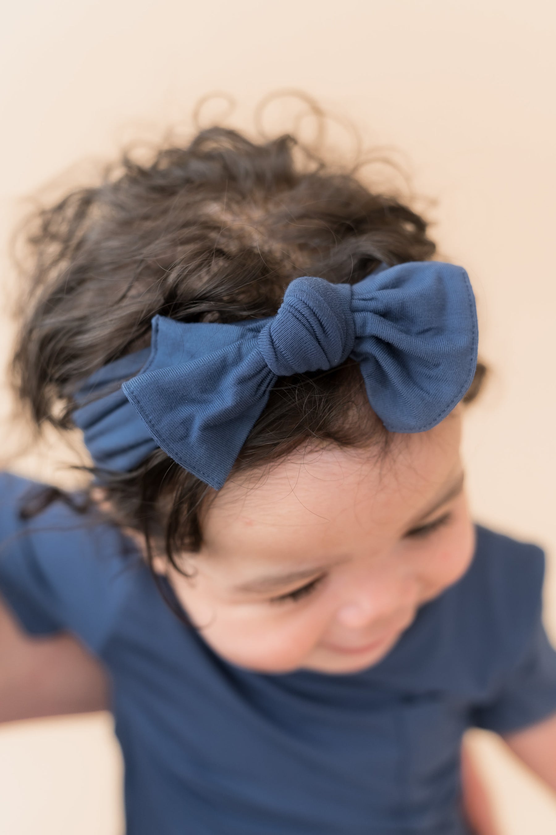 Baby wearing Knotted Bow Headband in Oxford on head over a beige background