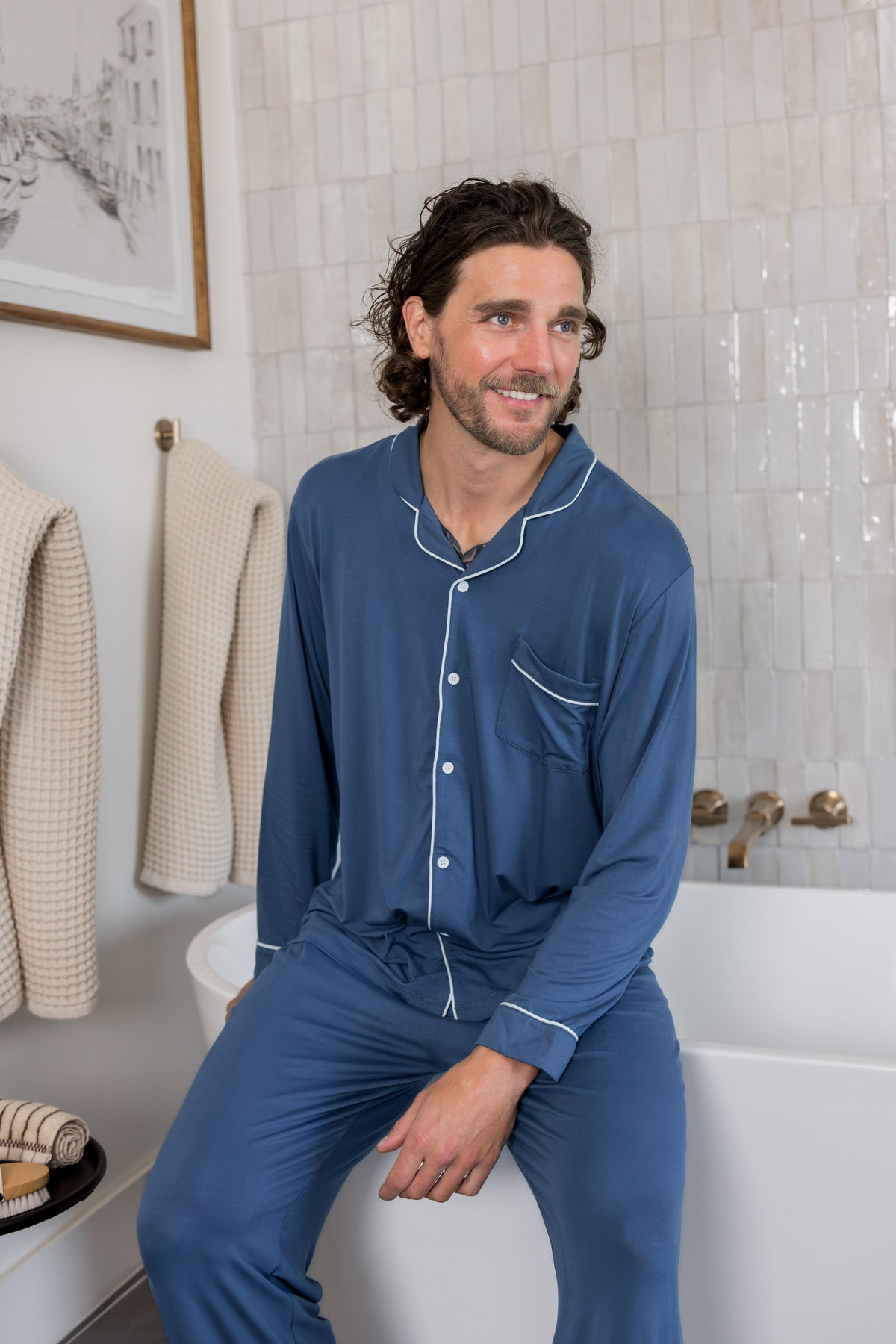 Model smiling in Men's Long Sleeve Pajama Set in Oxford sitting on the edge of bath tub