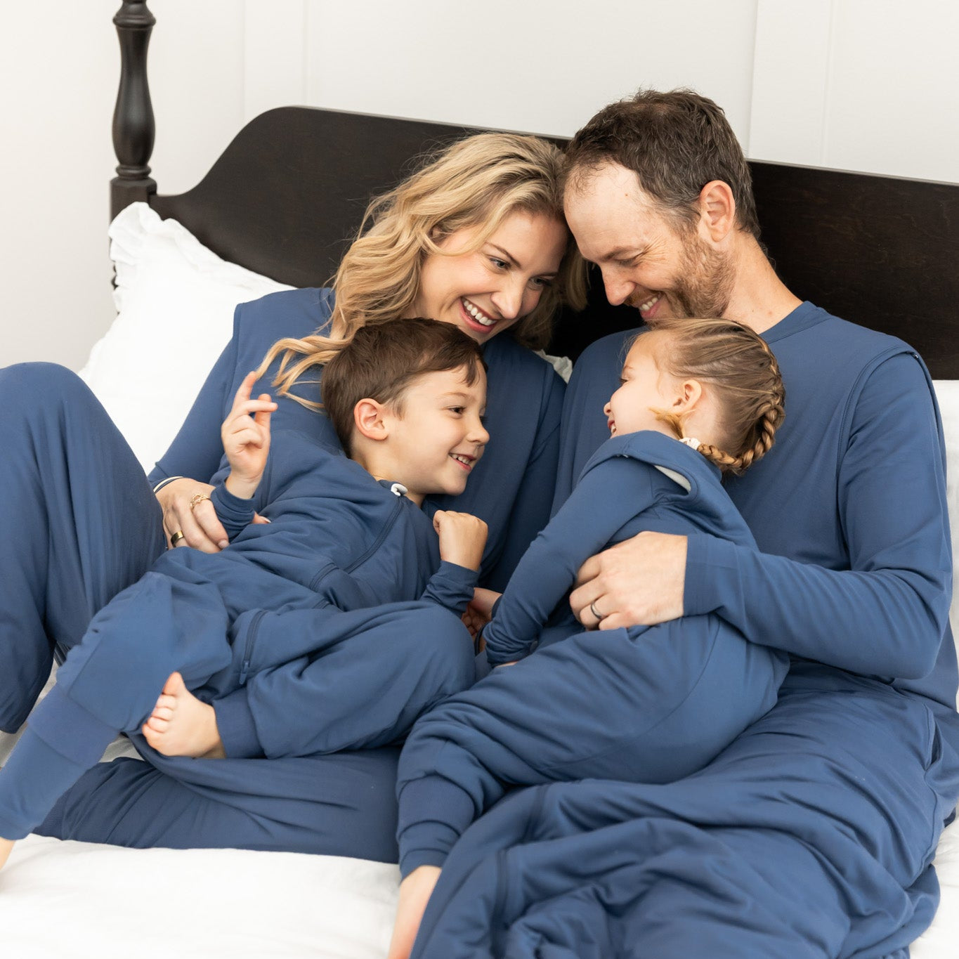 Family of  snuggled in bed wearing matching sleep bag walkers in a dark blue color