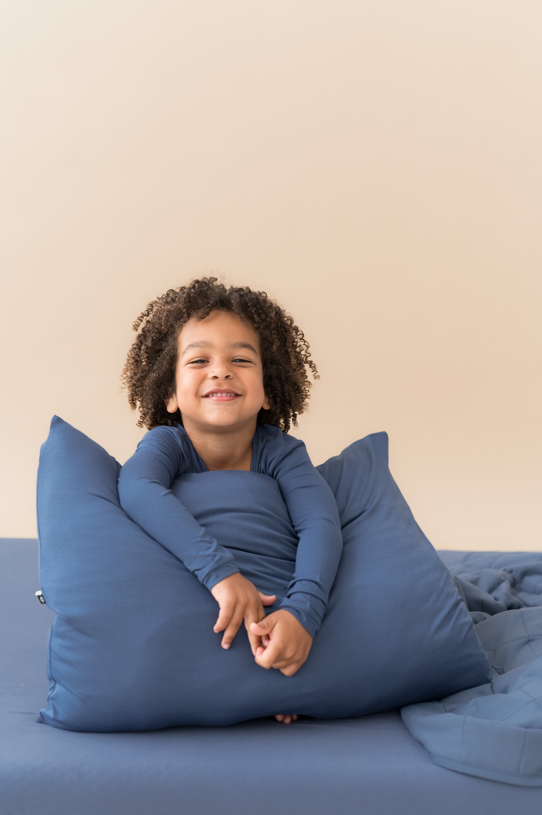 Boy holding Standard Pillowcase in Oxford sitting on a bed with similar color sheet and blanket