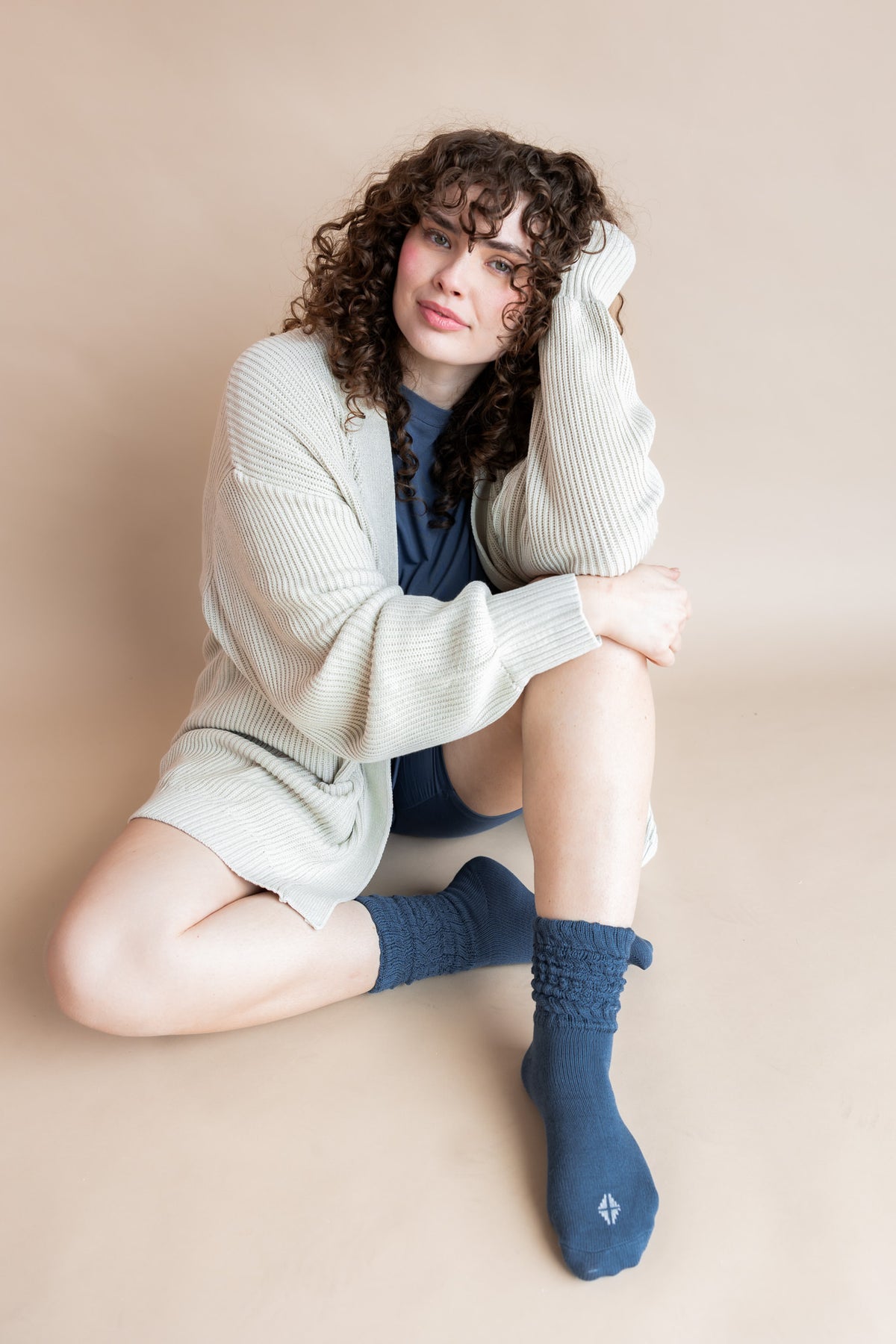 Model posing in Women’s Biker Short Set in Oxford with Adult Socks in Oxford and Oversized Chunky Knit Cardigan sitting on a beige background
