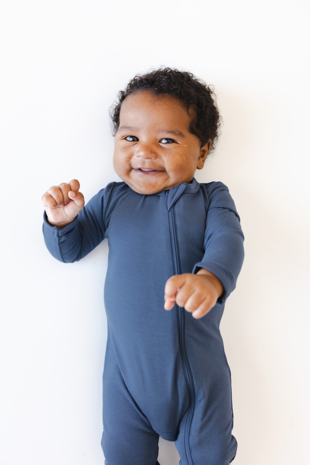 A smiling baby wearing a navy blue long-sleeve footless romper, standing against a plain white background.