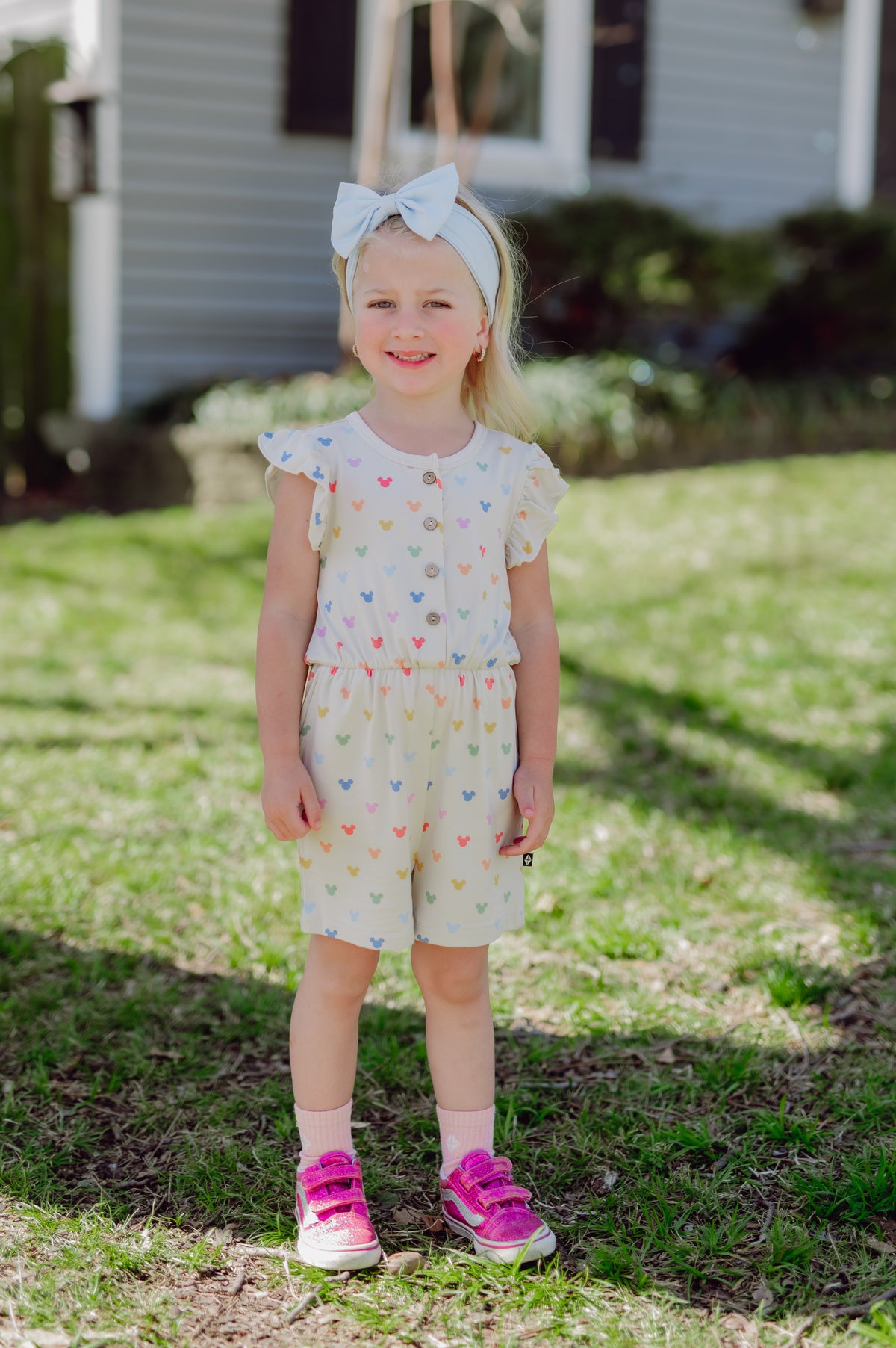 Young girl wearing a romper with wooden buttons and a mickey mouse colorful pattern