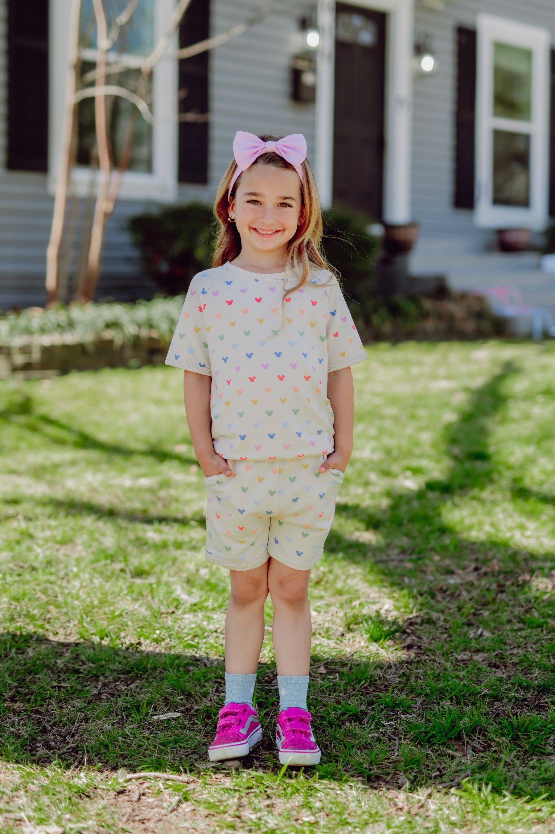 Young girl standing in a grassy area wearing a colorful mickey-patterned outfit.