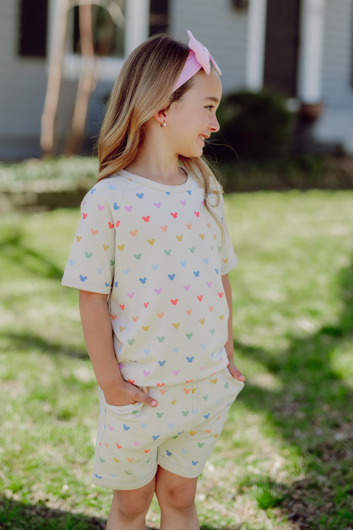Young girl wearing a light-colored outfit with colorful mickey patterns outdoors.
