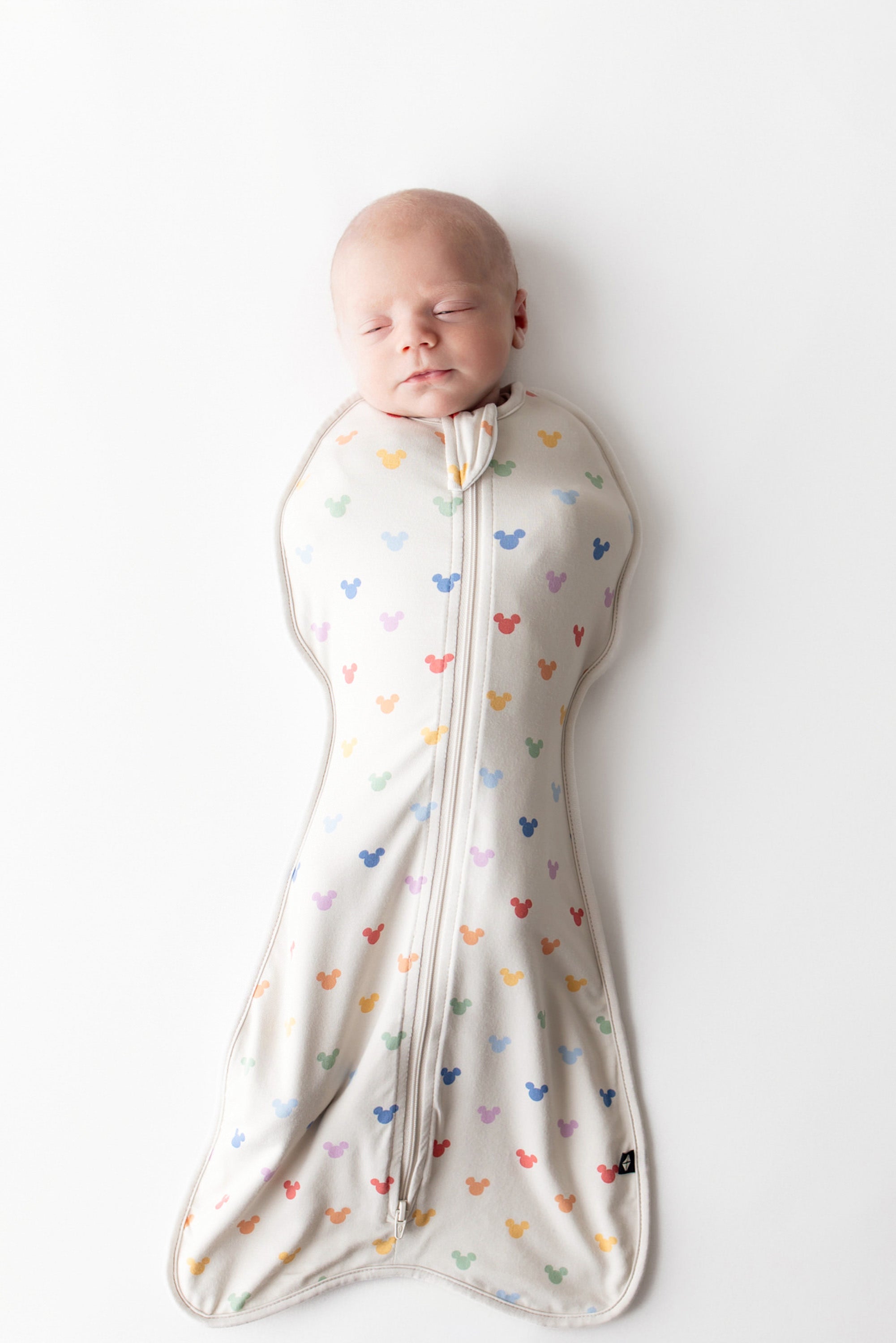 Baby asleep in kyte baby swaddle bag with pastel mickey head pattern