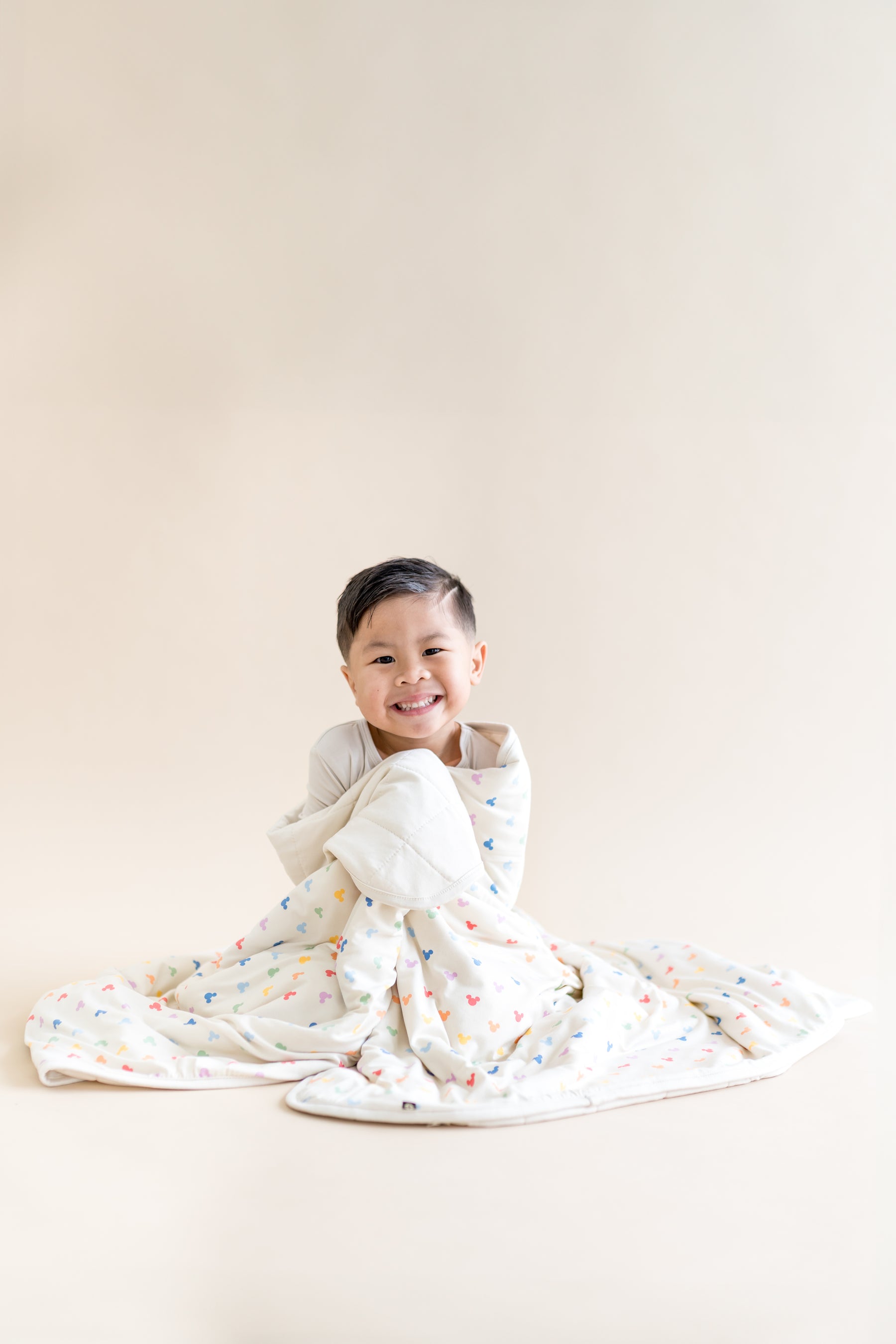 Child wrapped in a colorful blanket with mickey head pattern on a plain background