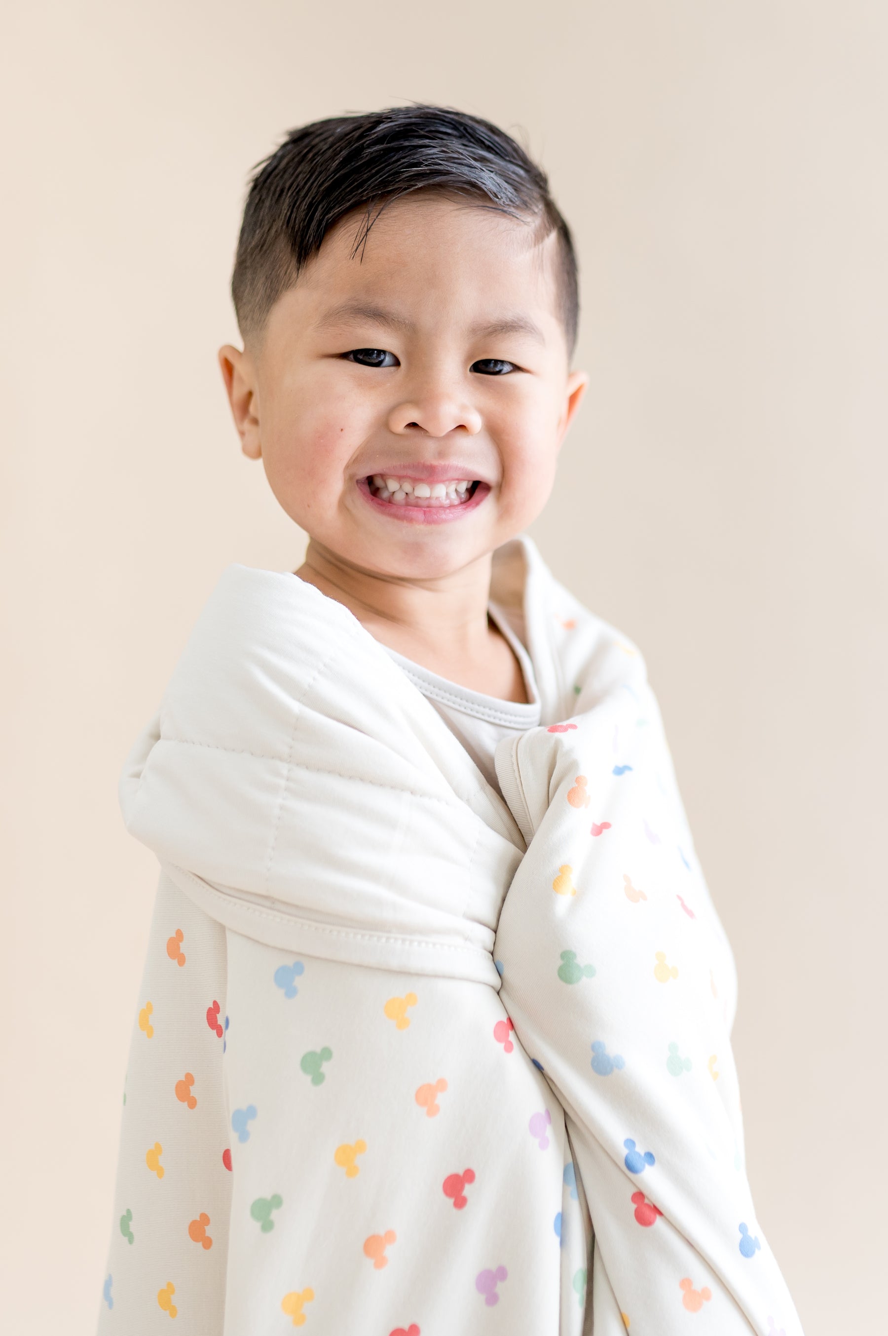Child wrapped in a blanket with colorful patterns on a plain background