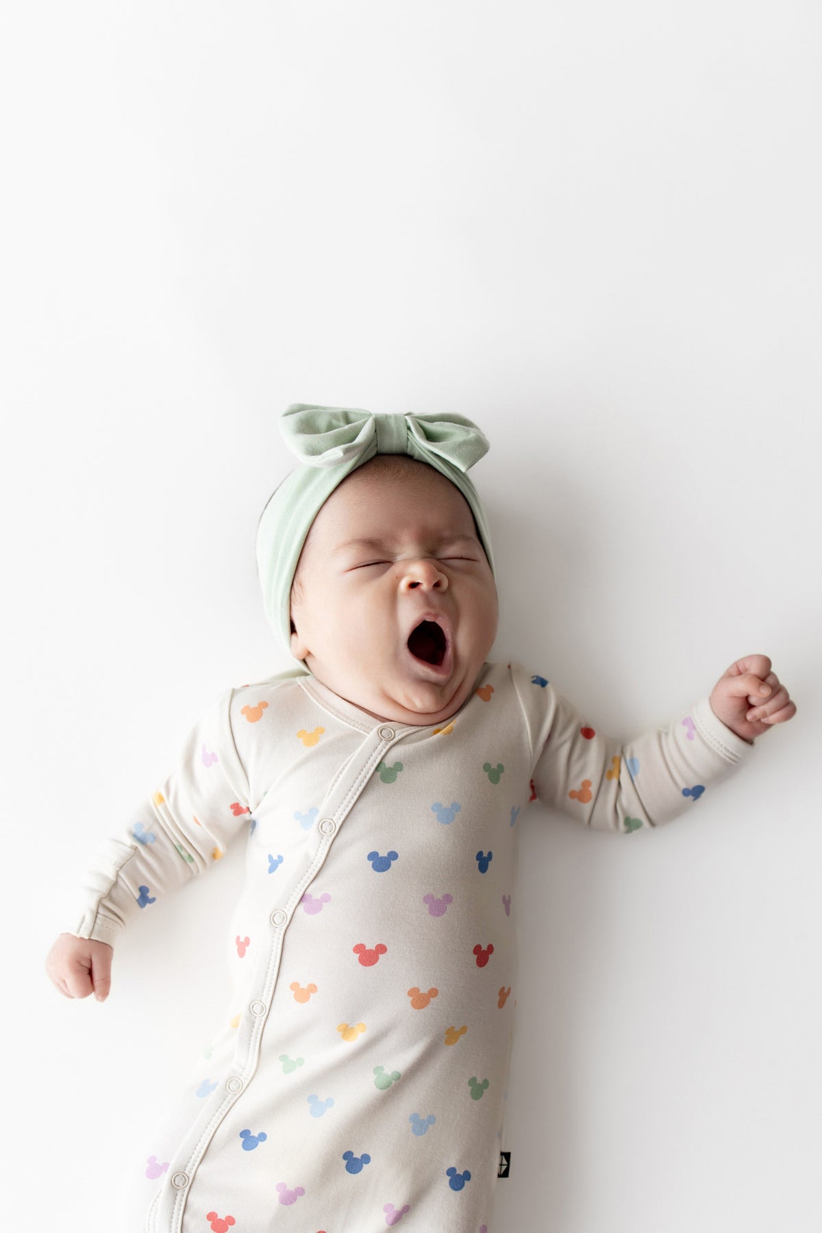 Baby yawning wearing a Mickey Mouse printed bundler and green bow