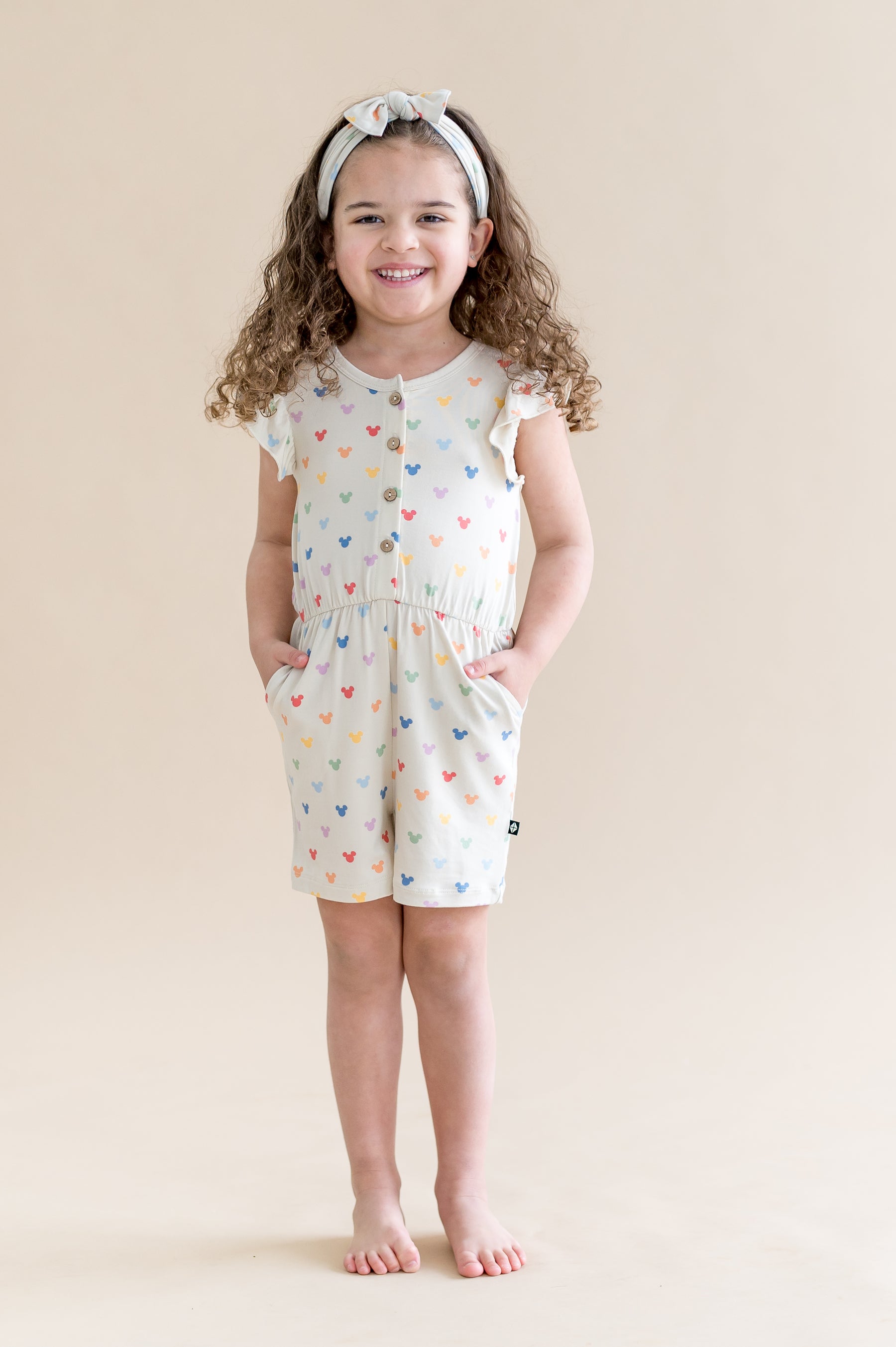 Child wearing cream flutter sleeve romper with a pastel mickey head print