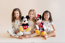 3 kids sitting with mickey and friends printed pajamas holding mickey and minnie mouse stuffed characters
