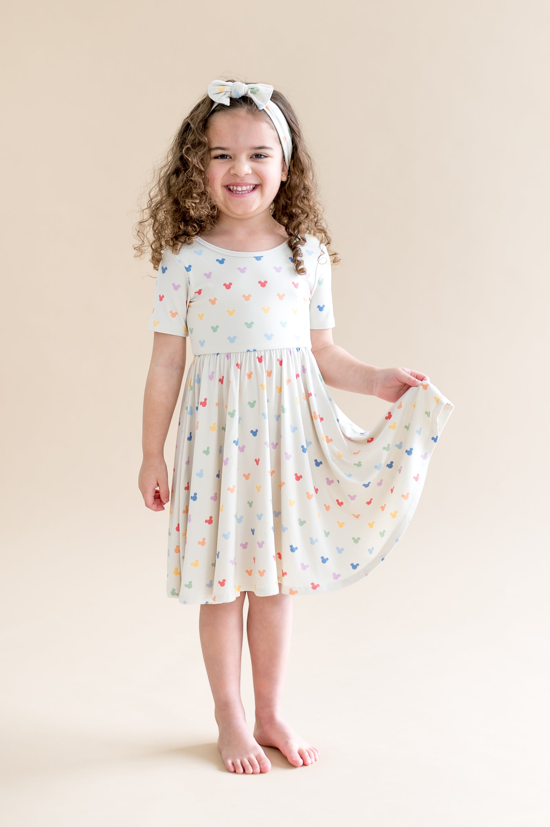 Girl in a short sleeve cream dress with  colorful mickey mouse head pattern 