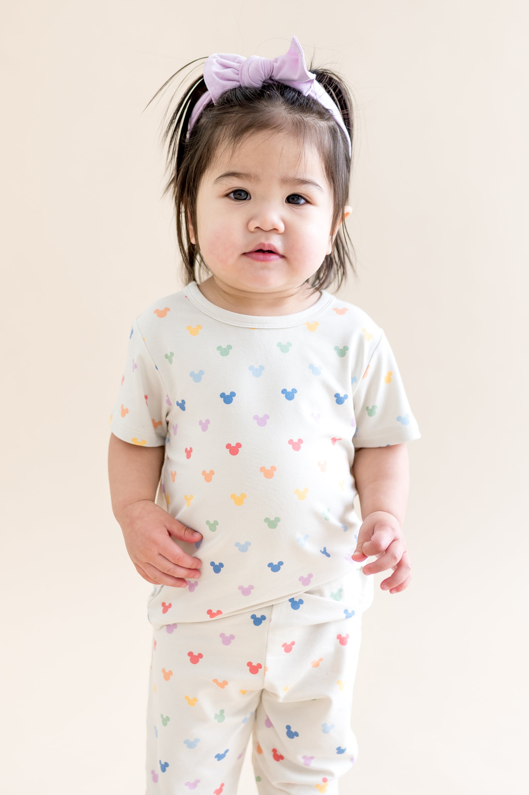 Child wearing a white outfit with colorful mickey patterns on a plain background