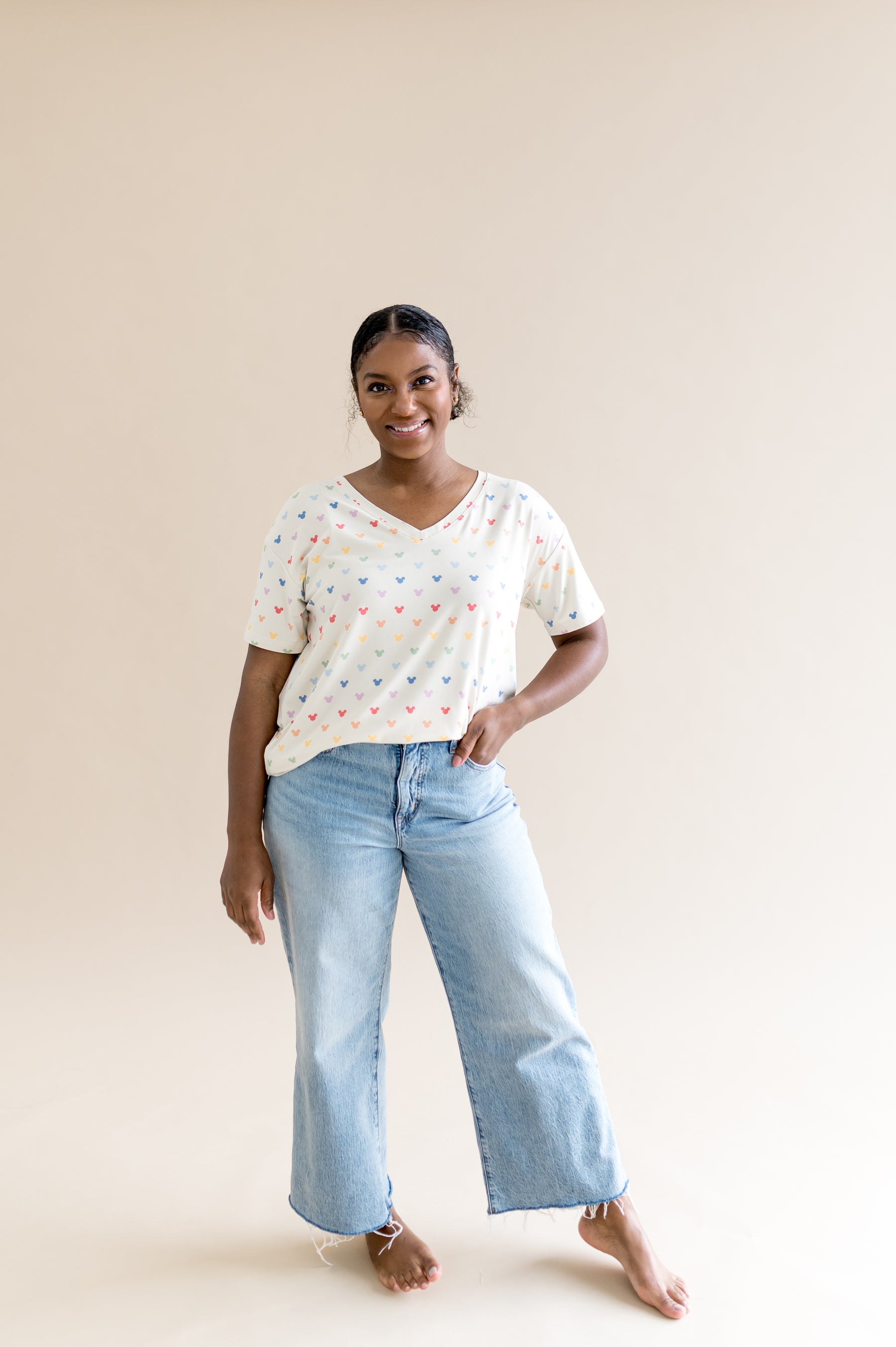 Woman wearing a cream oversized v-neck with colorful patterns and light blue jeans on a beige background