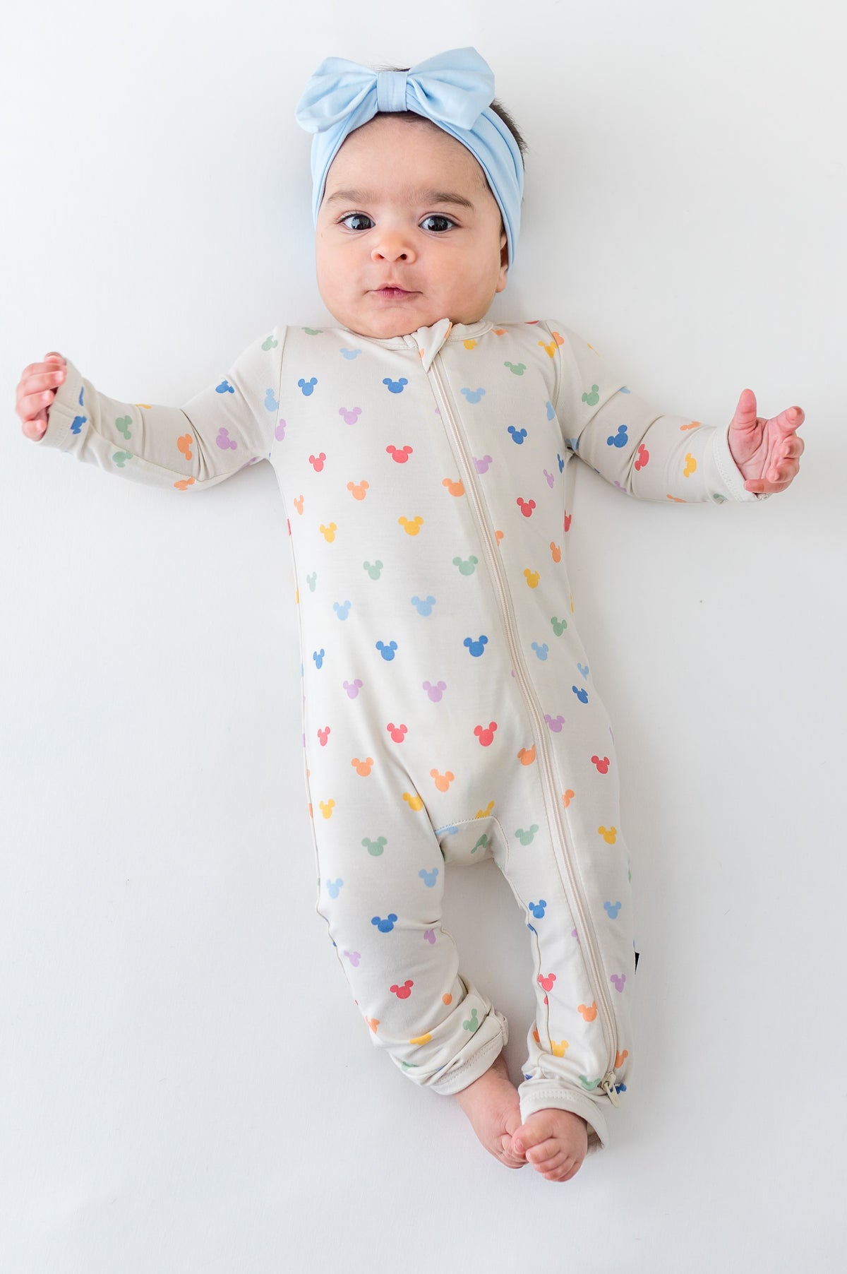 Baby in a colorful mickey head printed zippered romper and blue bow