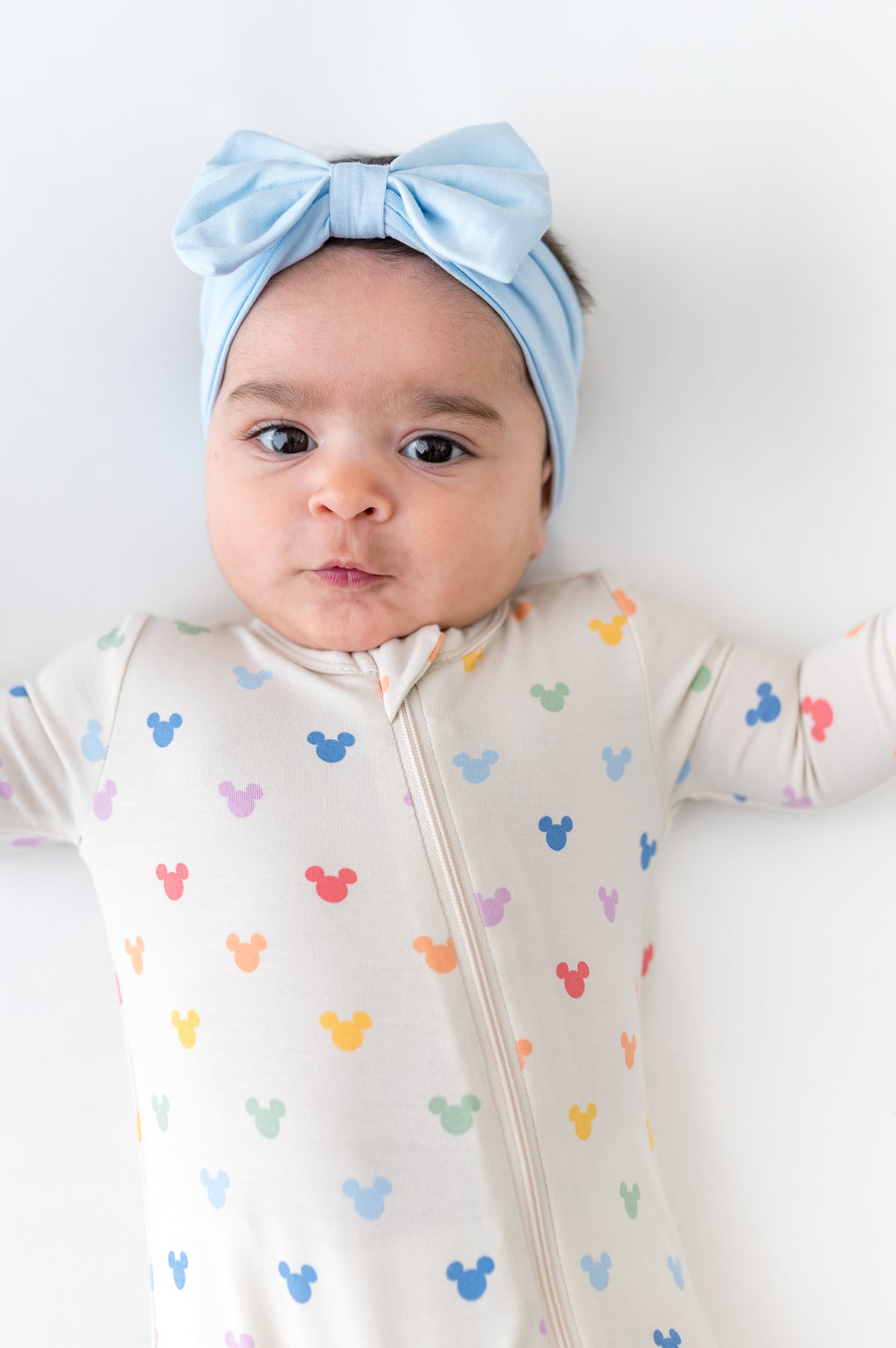 Baby wearing a zippered romper with mickey head pattern and blue bow
