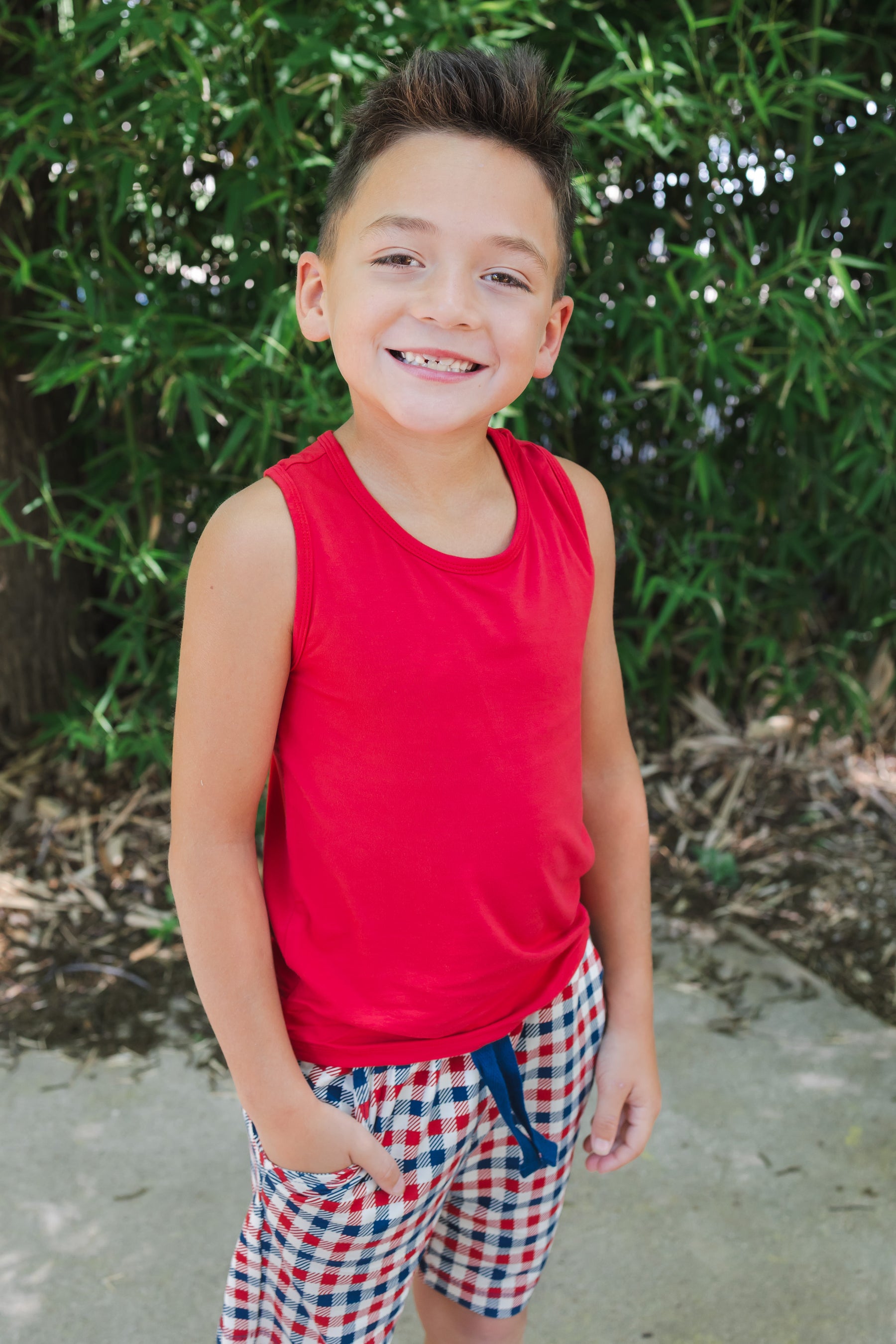 Child smiling wearing a Cardinal tank top over a red blue and white Patriotic Gingham check print drawstring shorts outdoors
