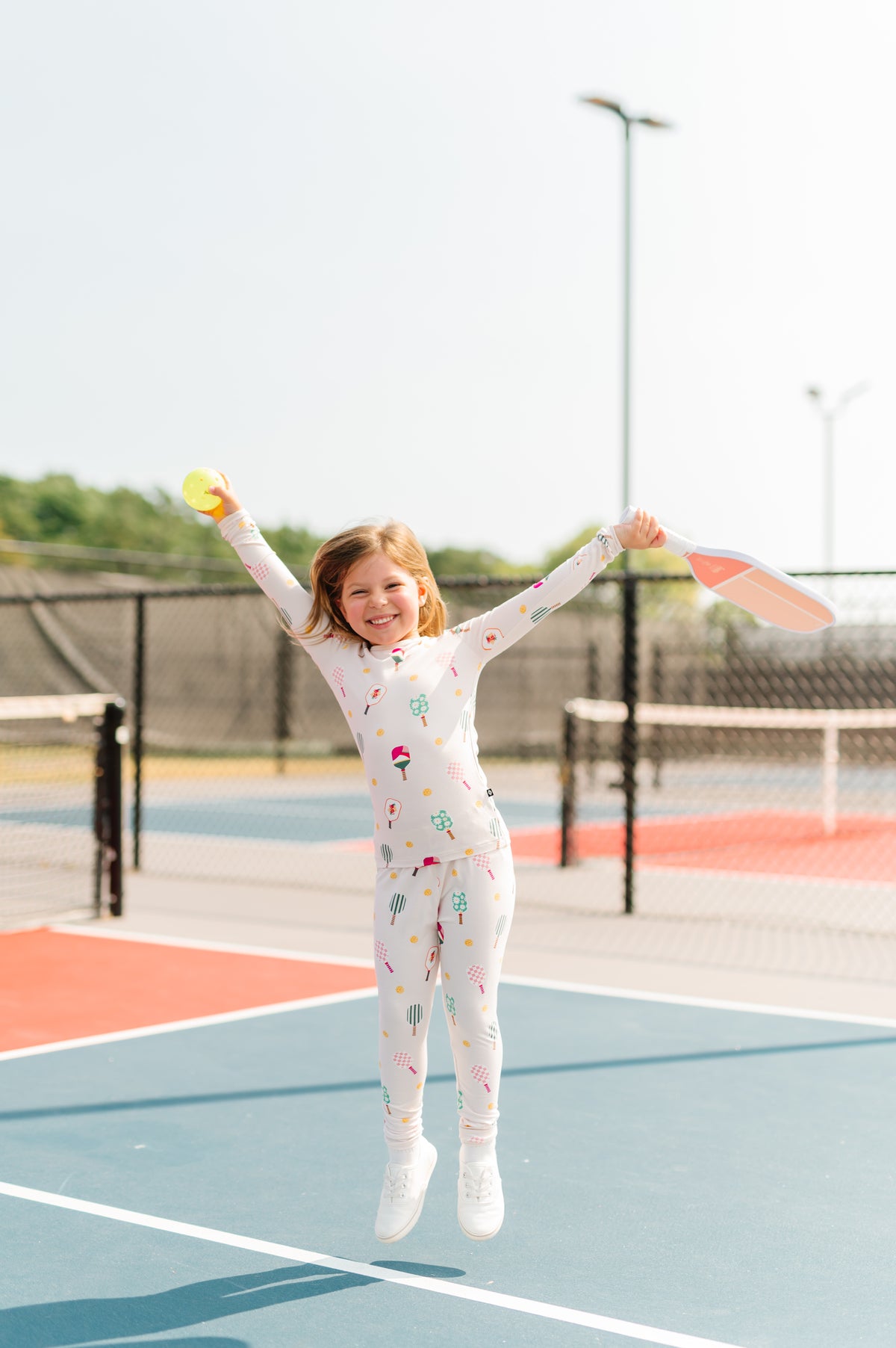 Girl jumping in Long Sleeve Pajamas in Pickleball print holding a ball