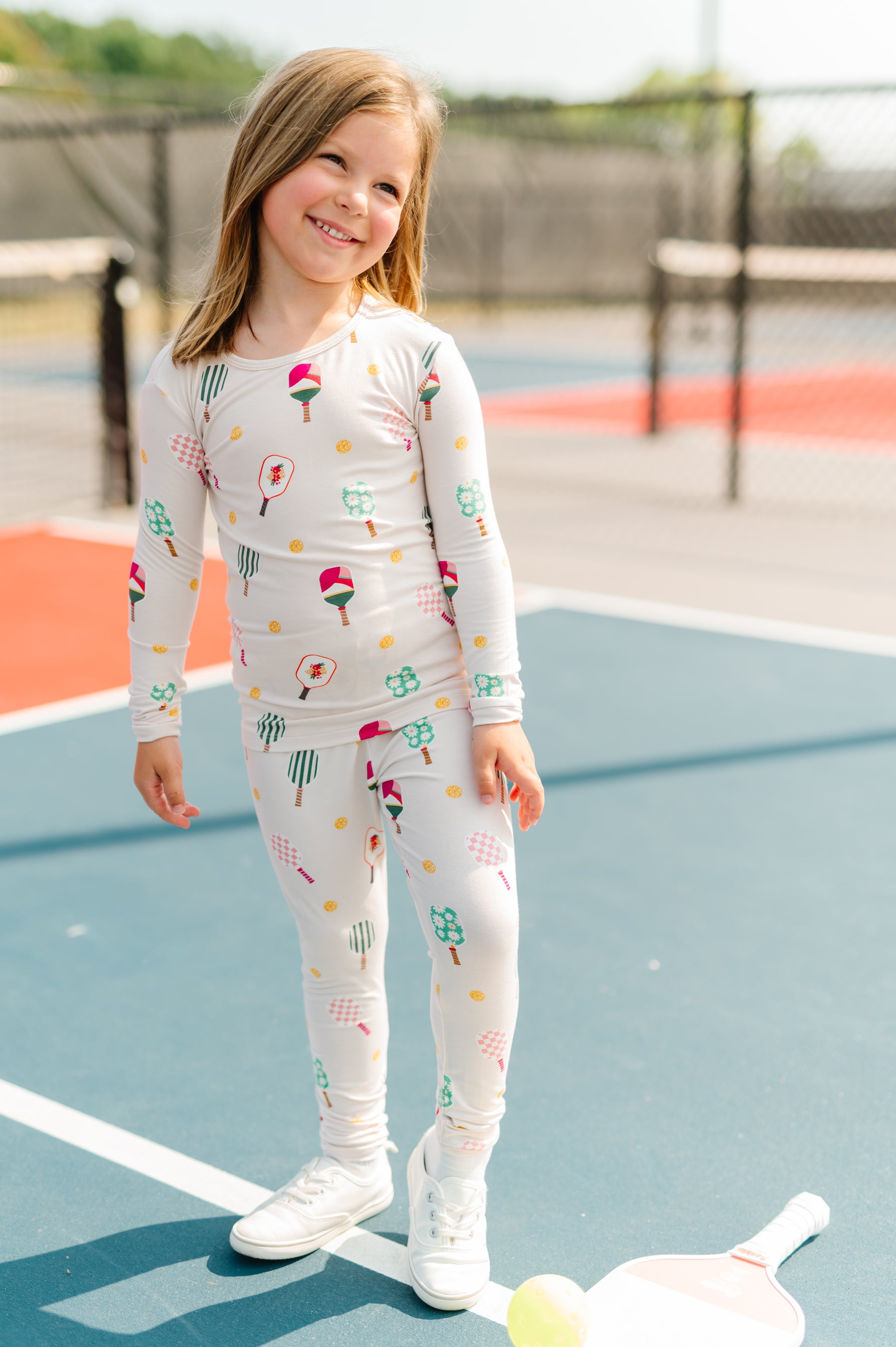 Girl poring in Long Sleeve Pajamas in Pickleball print standing on pickleball court