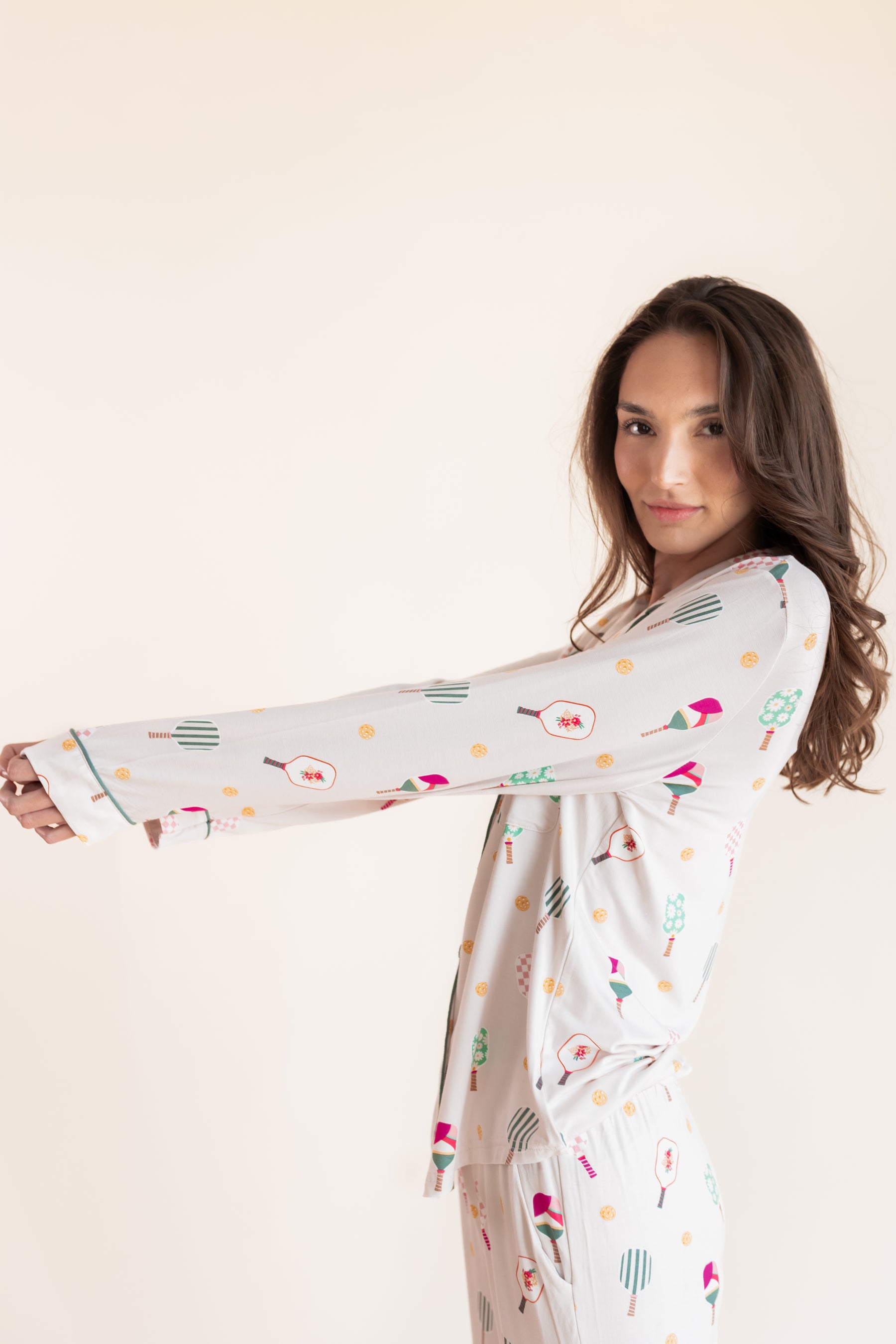 A woman modeling a long-sleeve white pajama set with a colorful pickleball  print, posed against a solid light beige background.