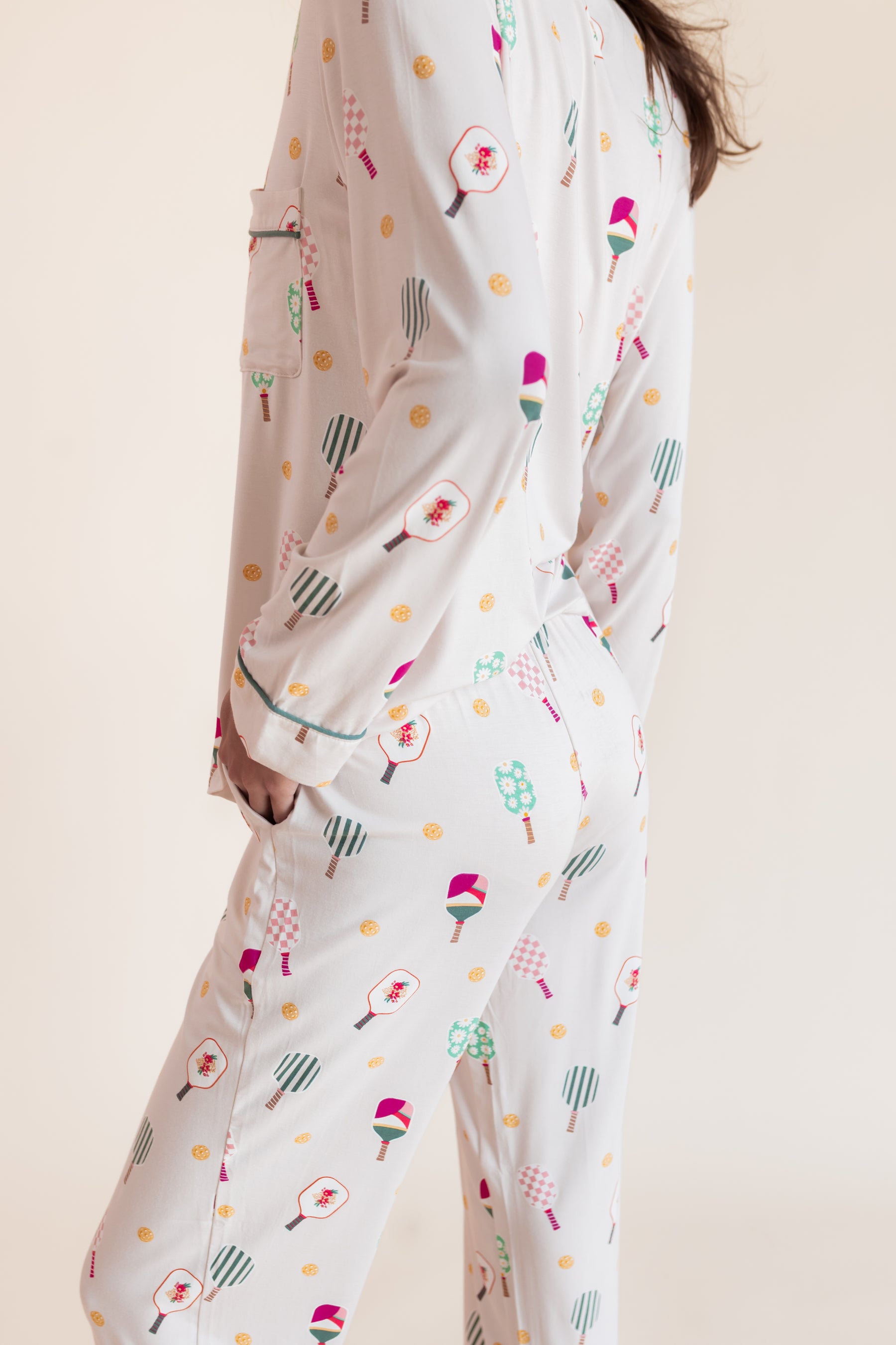 A person wearing a matching long-sleeve pajama set with a playful pickleball  print, shown from the back against a plain beige studio background.