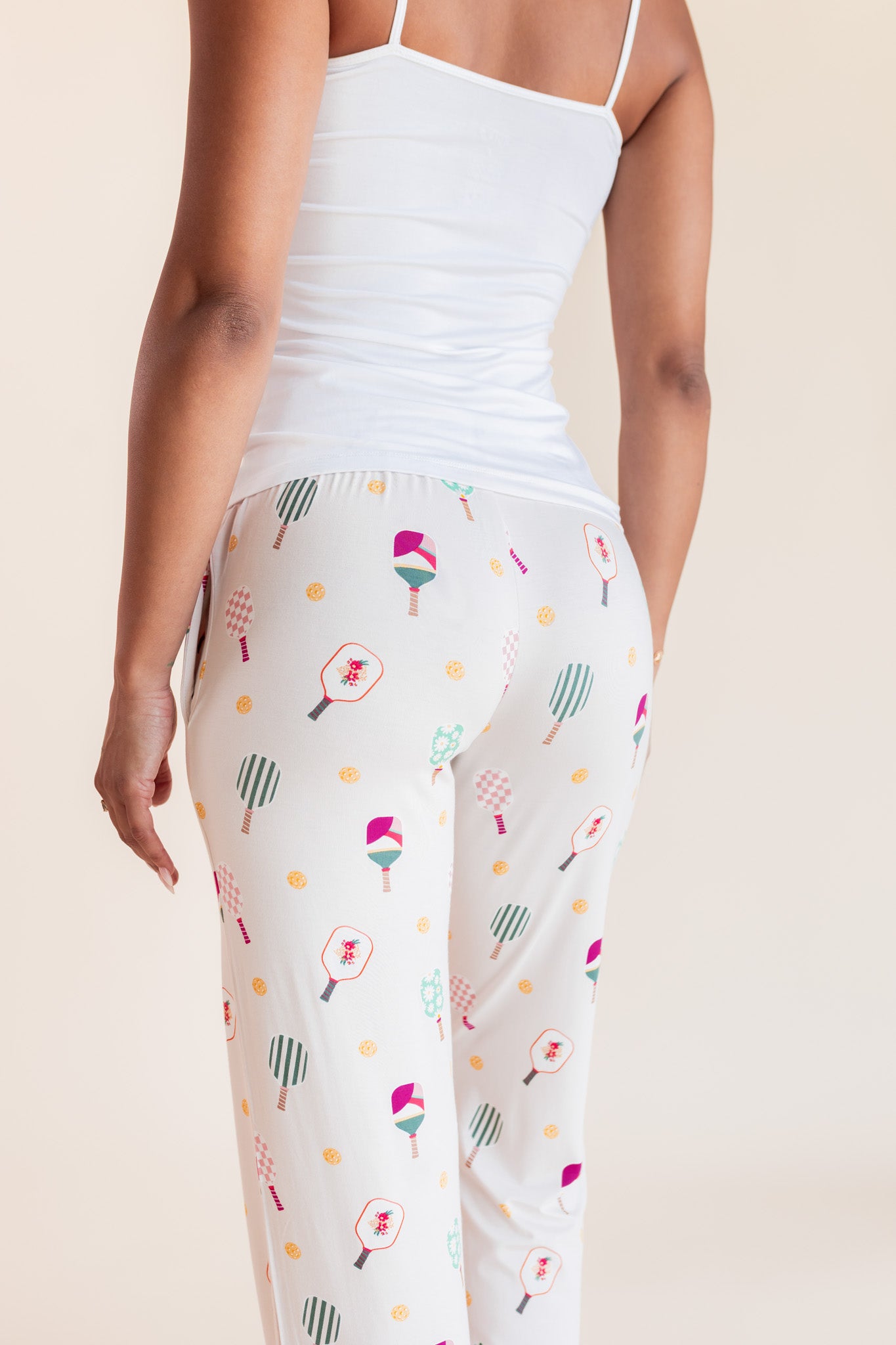 White leggings with a colorful pickleball racket pattern, worn by a model from the back against a light beige background.