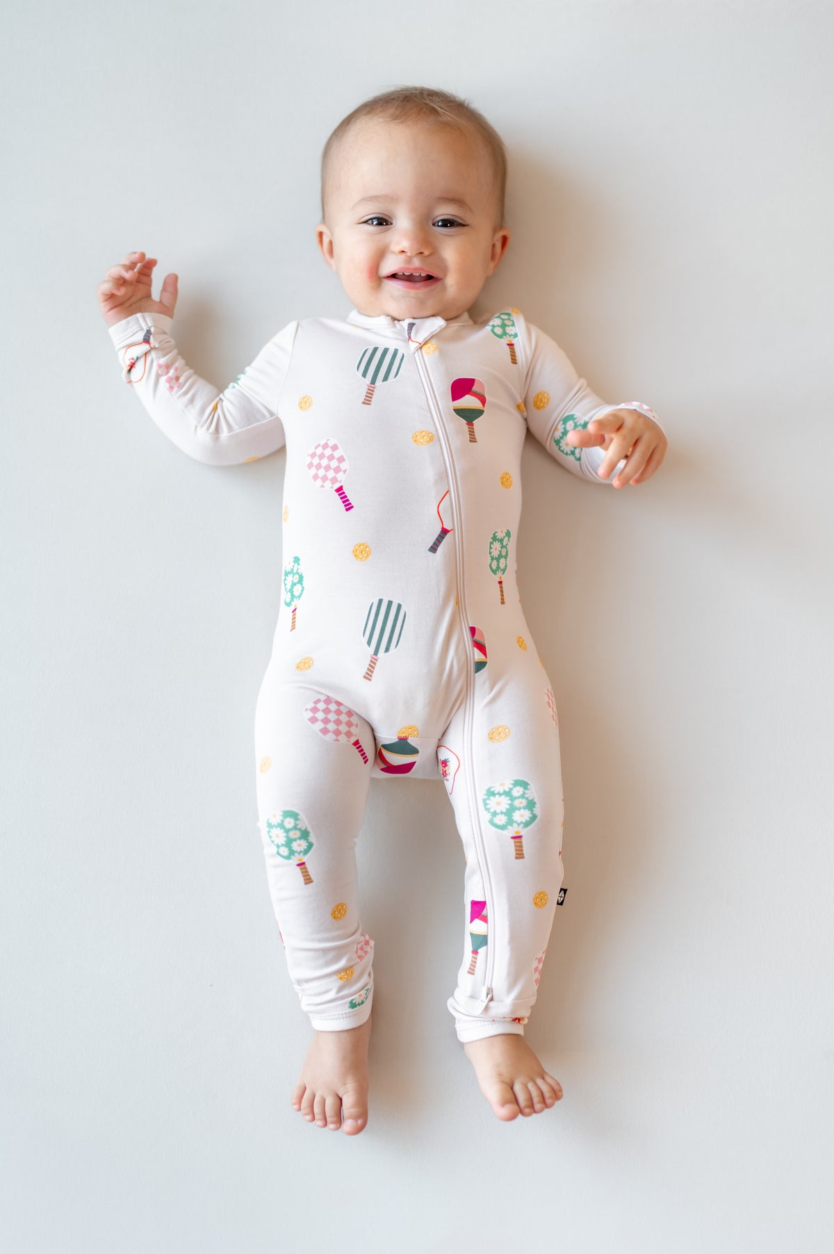 Baby lying on beige background wearing Zippered Romper in Pickleball print 
