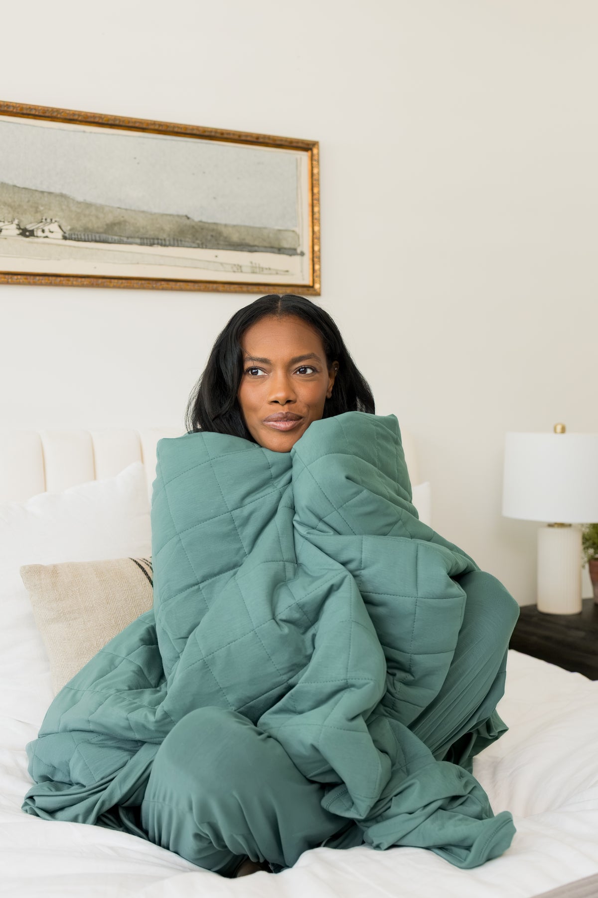 Model sitting on bed wrapped in Adult Quilted Blanket in Pine 2.5