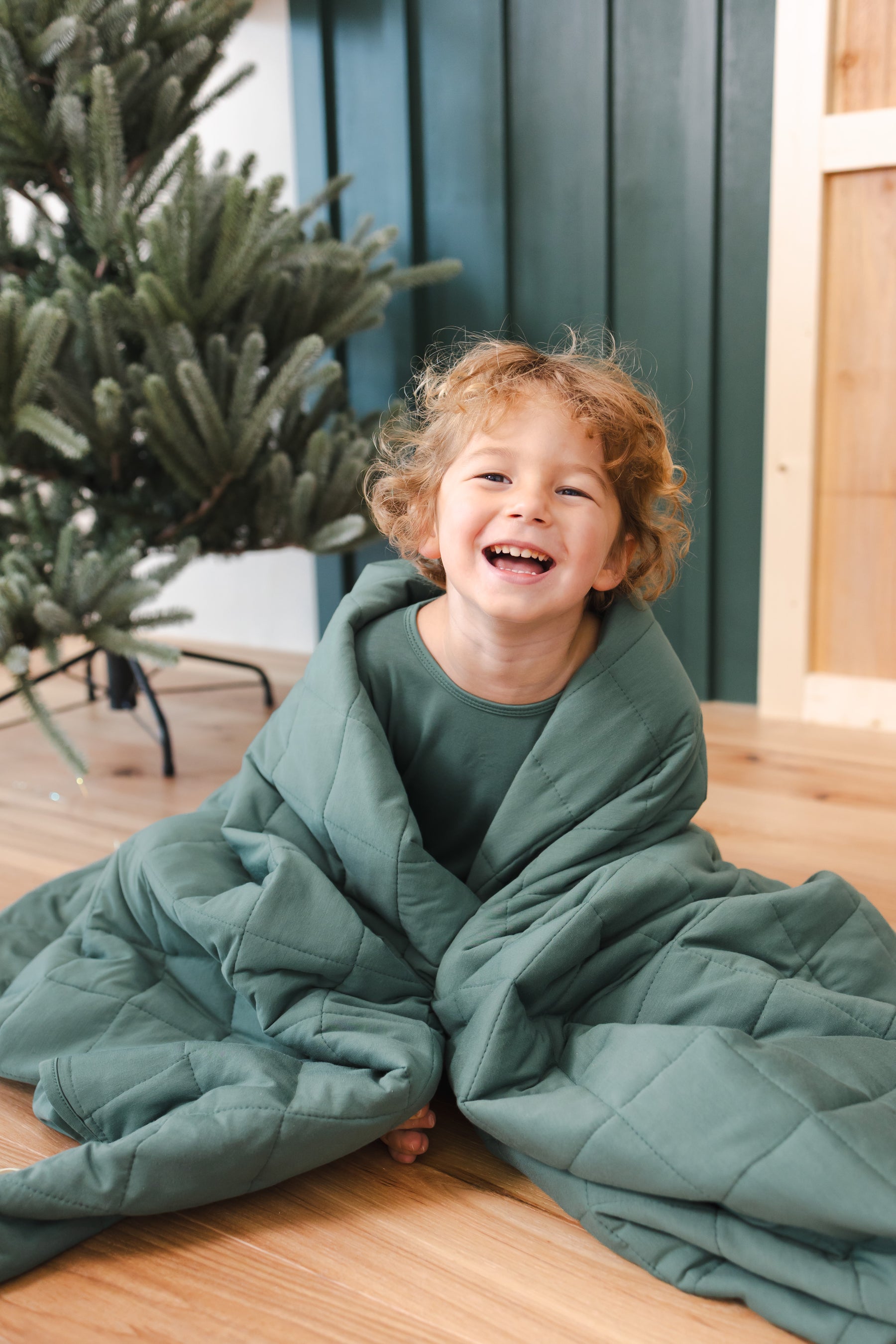 Toddler wrapped in Youth Blanket in Pine 2.5 sitting in on floor