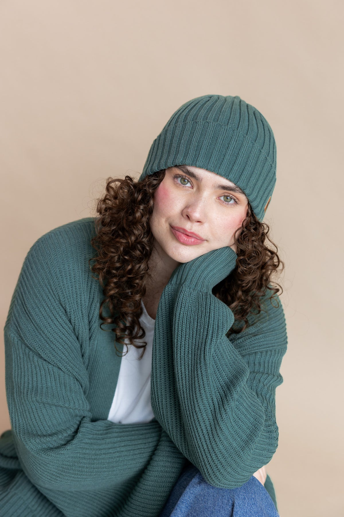 Modal wearing Chunky Knit Adult Ribbed Beanie in Pine over white T-shirt and Chunky knit cardigan in Pine on a beige background